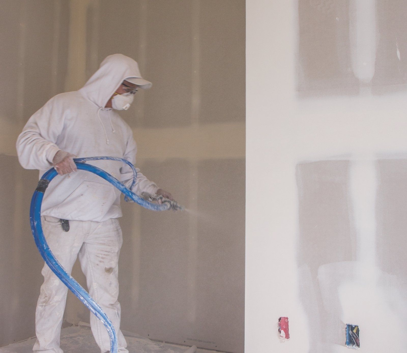 Person in white protective gear spraying drywall.