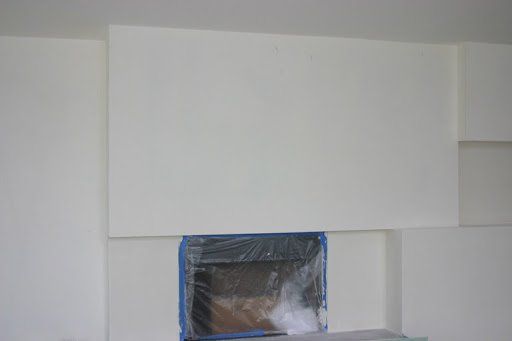White wall with a rectangular covering above a fireplace opening, taped with blue tape.