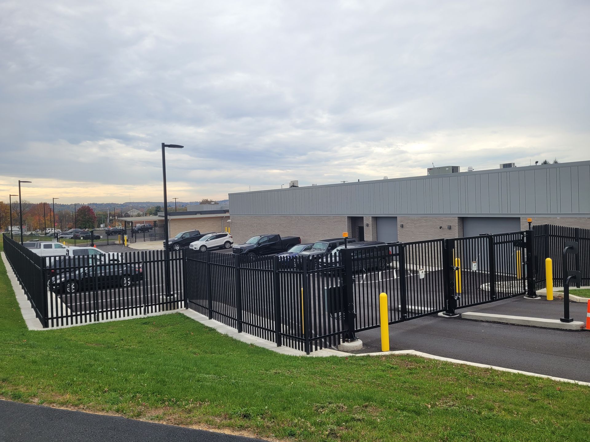 Black metal fence along a parking lot beside a gray industrial building under a cloudy sky