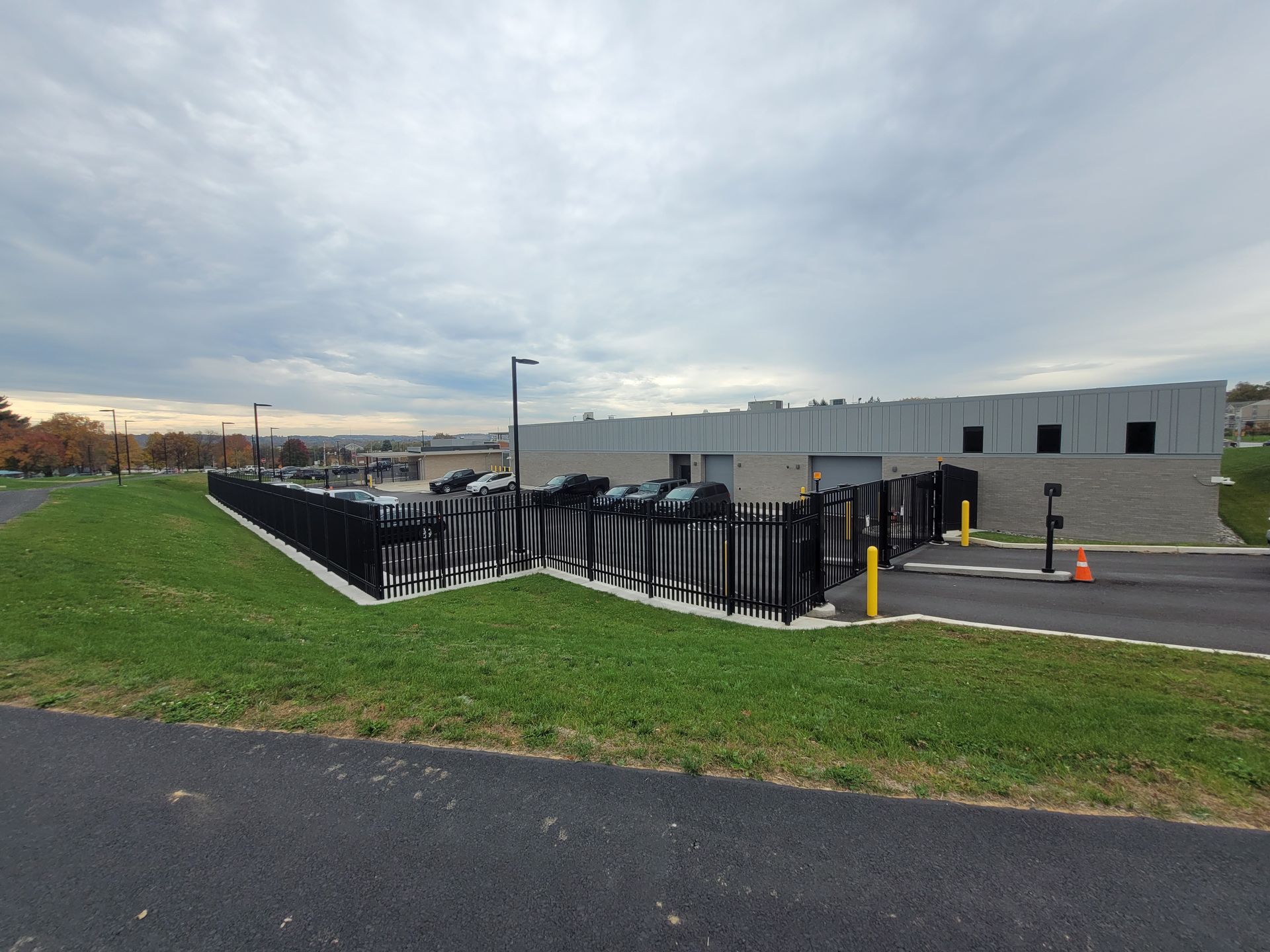 Parking lot with black fencing and a gray building under a cloudy sky.