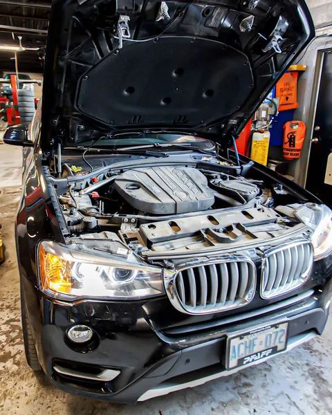 Black BMW SUV with open hood in a garage.