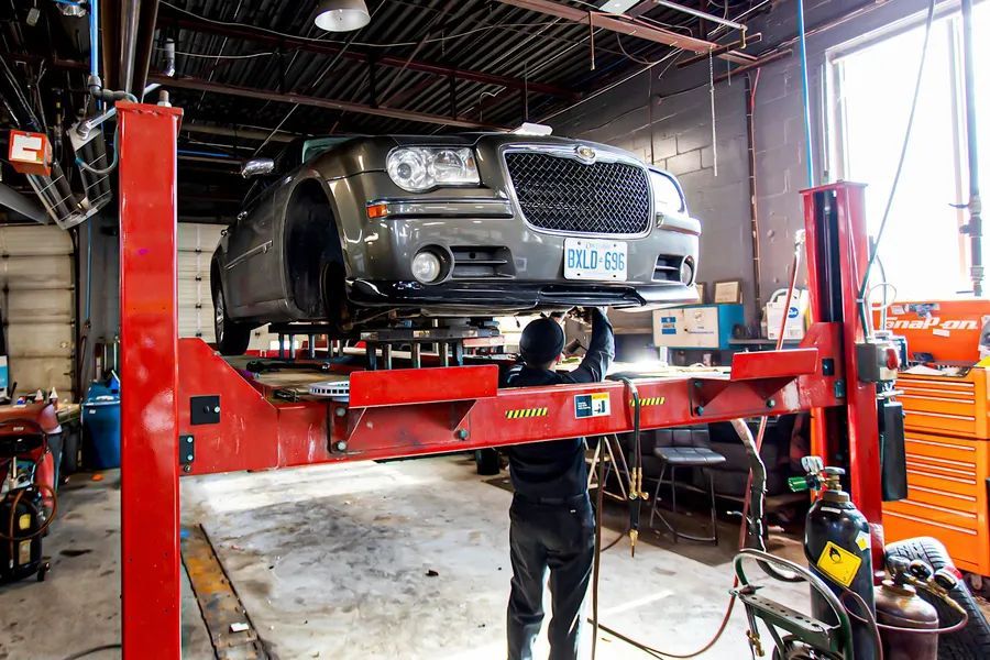 Car on a lift in a garage, a mechanic working underneath; red lift, gray car, tools.