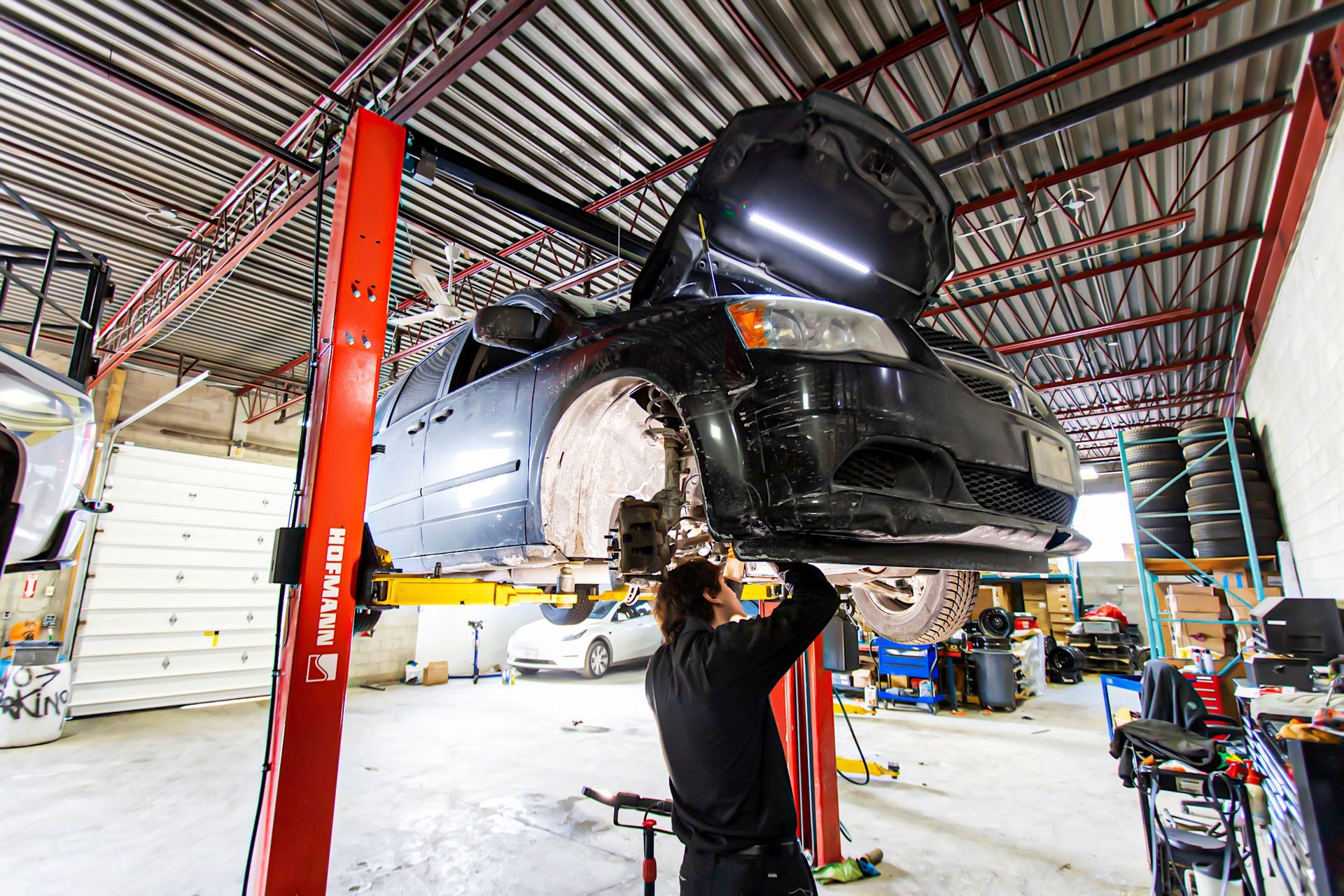 Mechanic working under a black car lifted on a hoist in a garage.