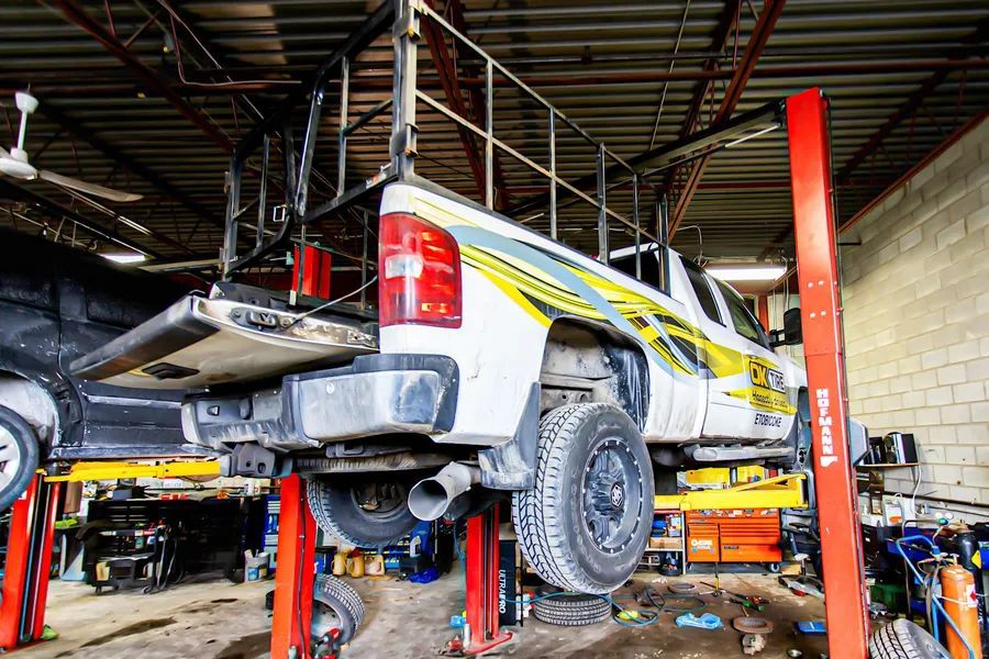 White pickup truck raised on a lift in a garage. Yellow and black decal on side.