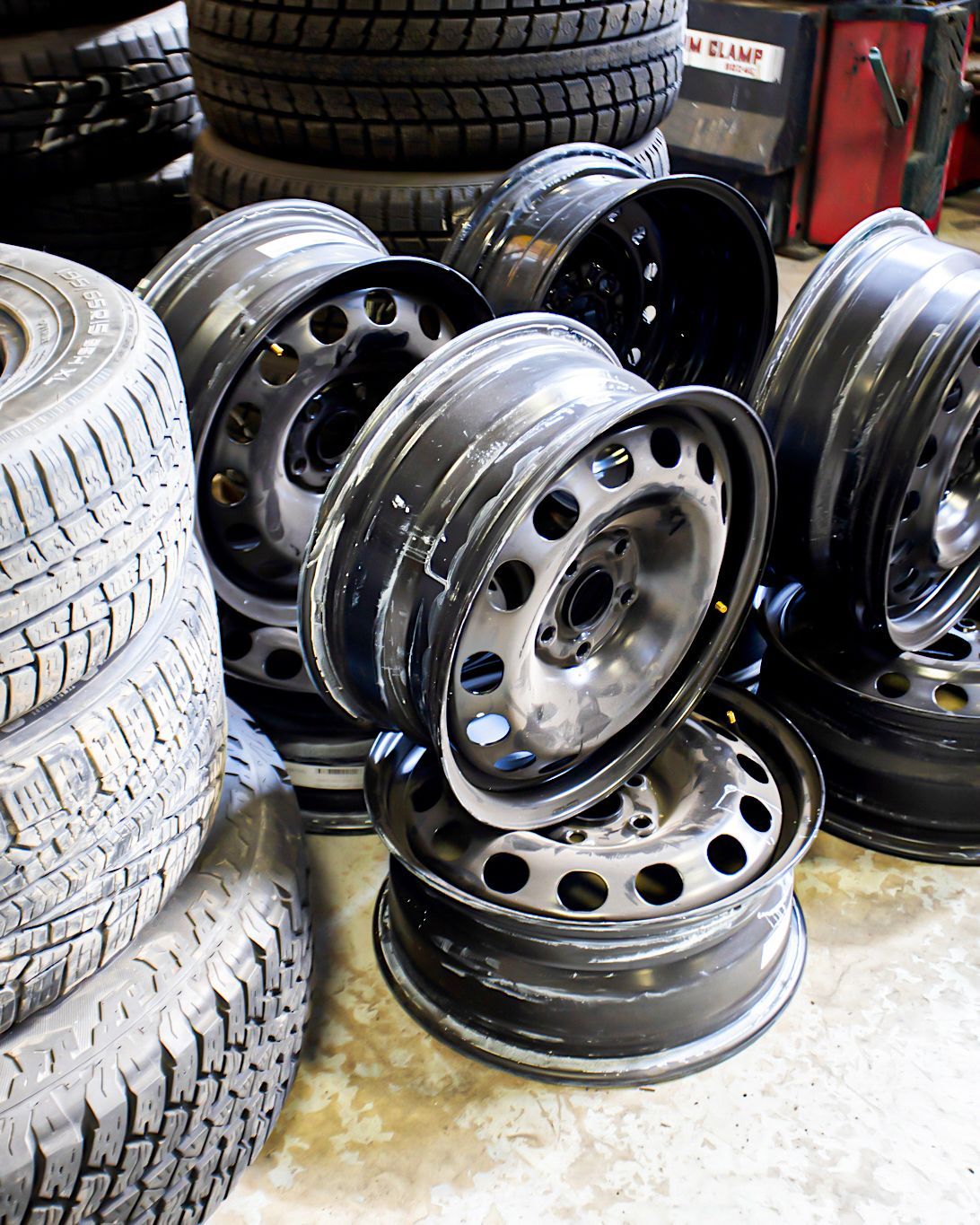 Tires stacked with black steel rims, in a garage or workshop setting.
