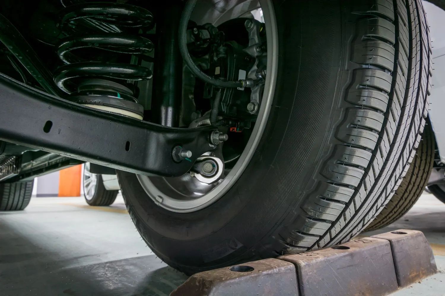 Car tire resting on a parking curb, suspension components visible.