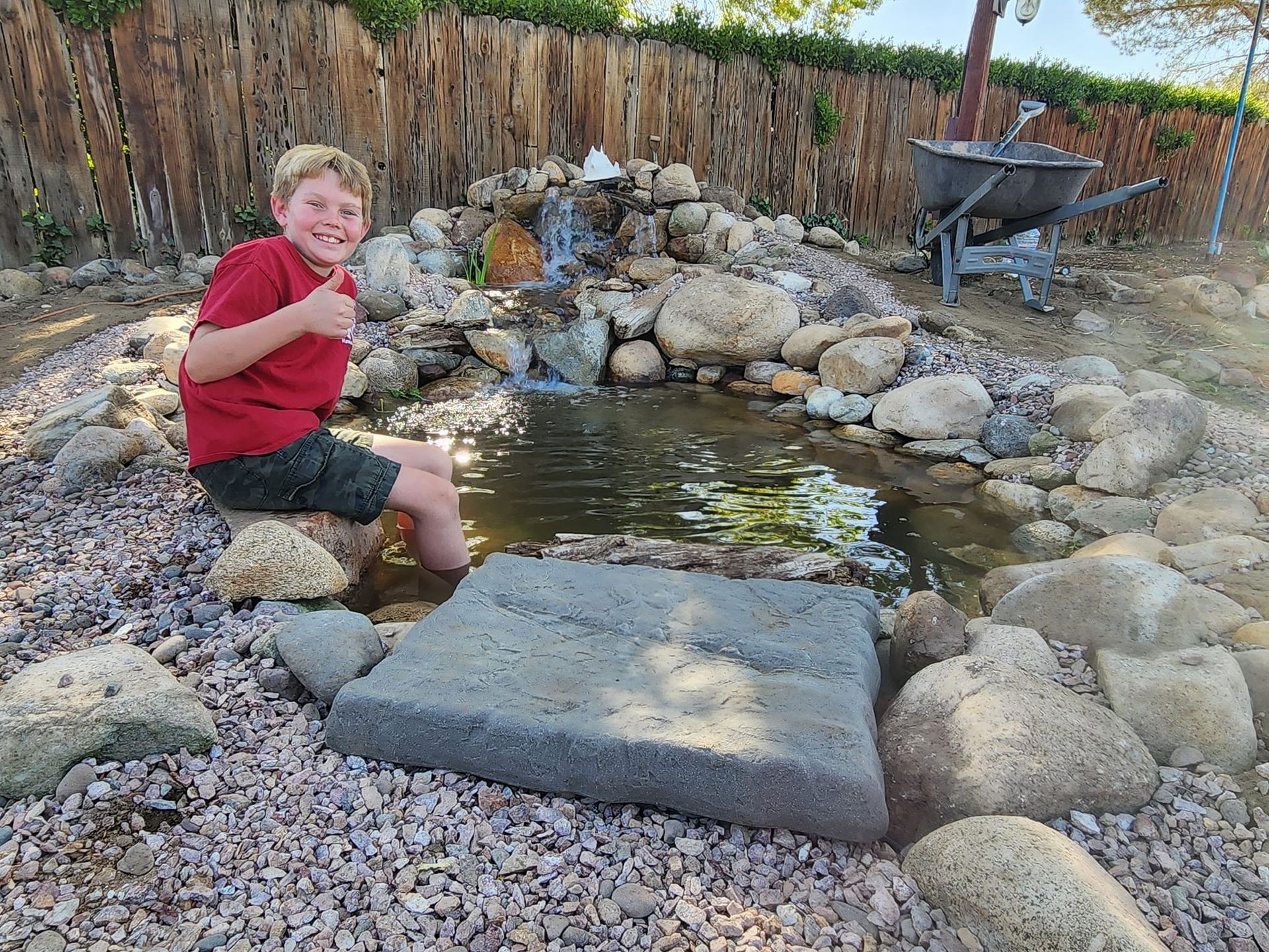 A young boy is sitting on a rock in front of a pond.
