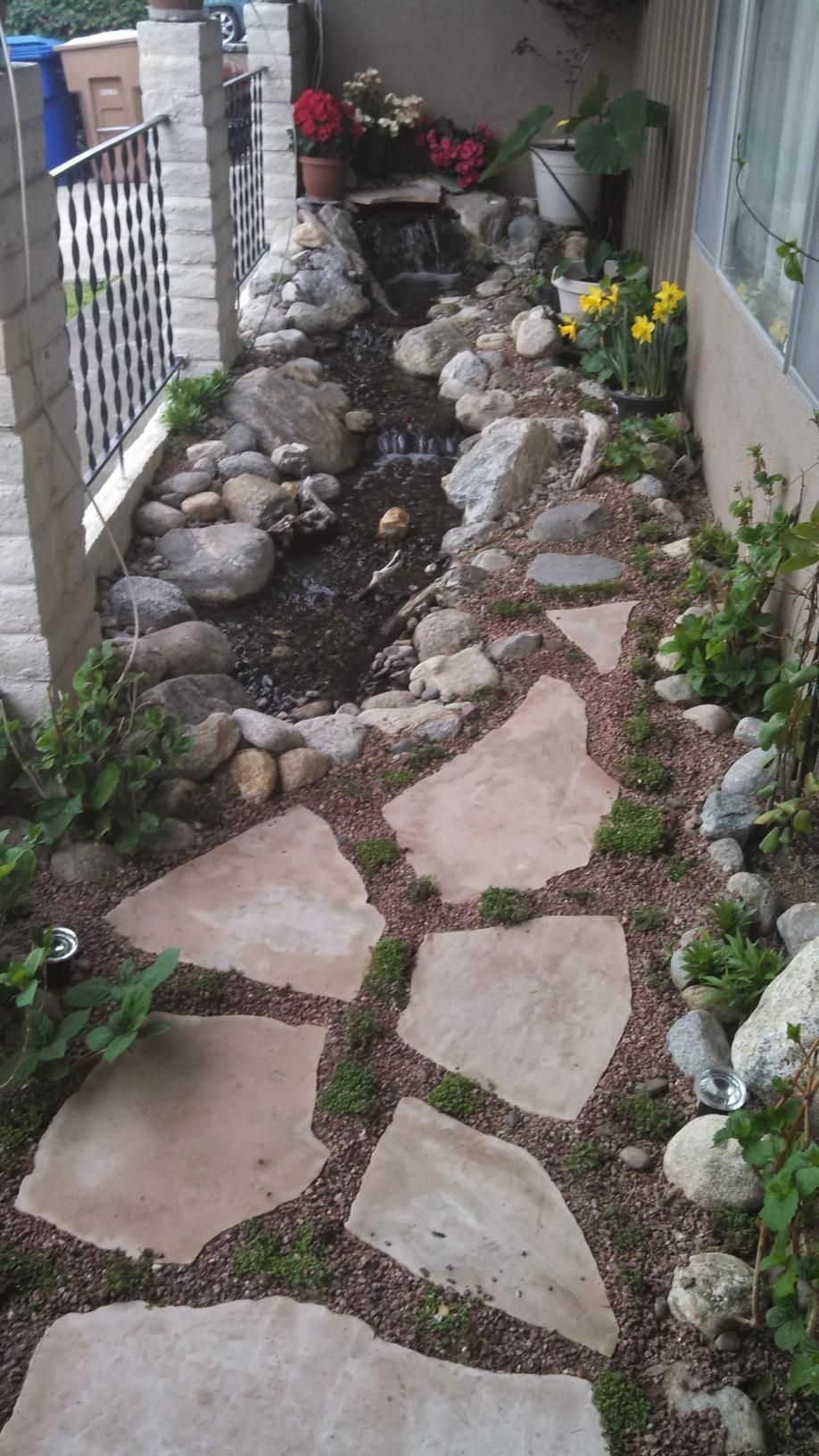 A stone walkway leading to a waterfall in a garden.