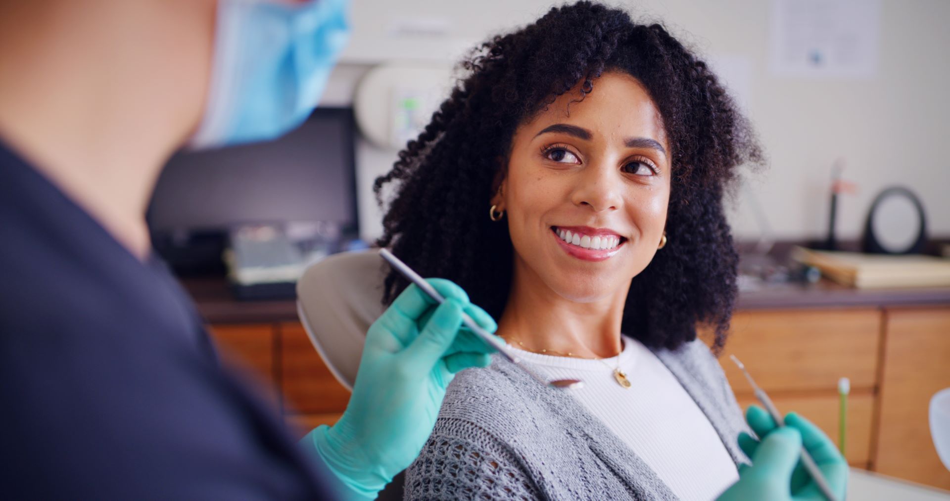 Dental patient smiling at dentist holding tools in a clinic examination room