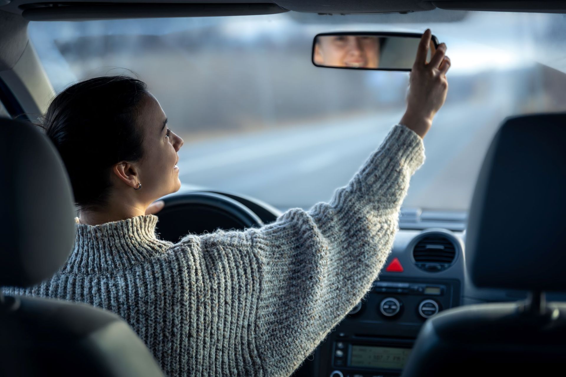 woman checking rearview mirror inside car smiling
