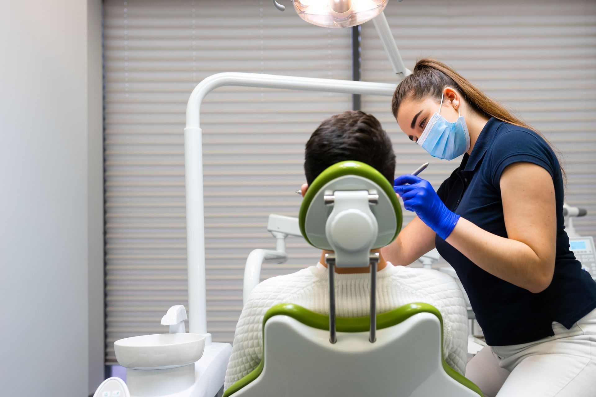 Man at dental check-up in chair with back towards us, while woman dental professional examining teeth