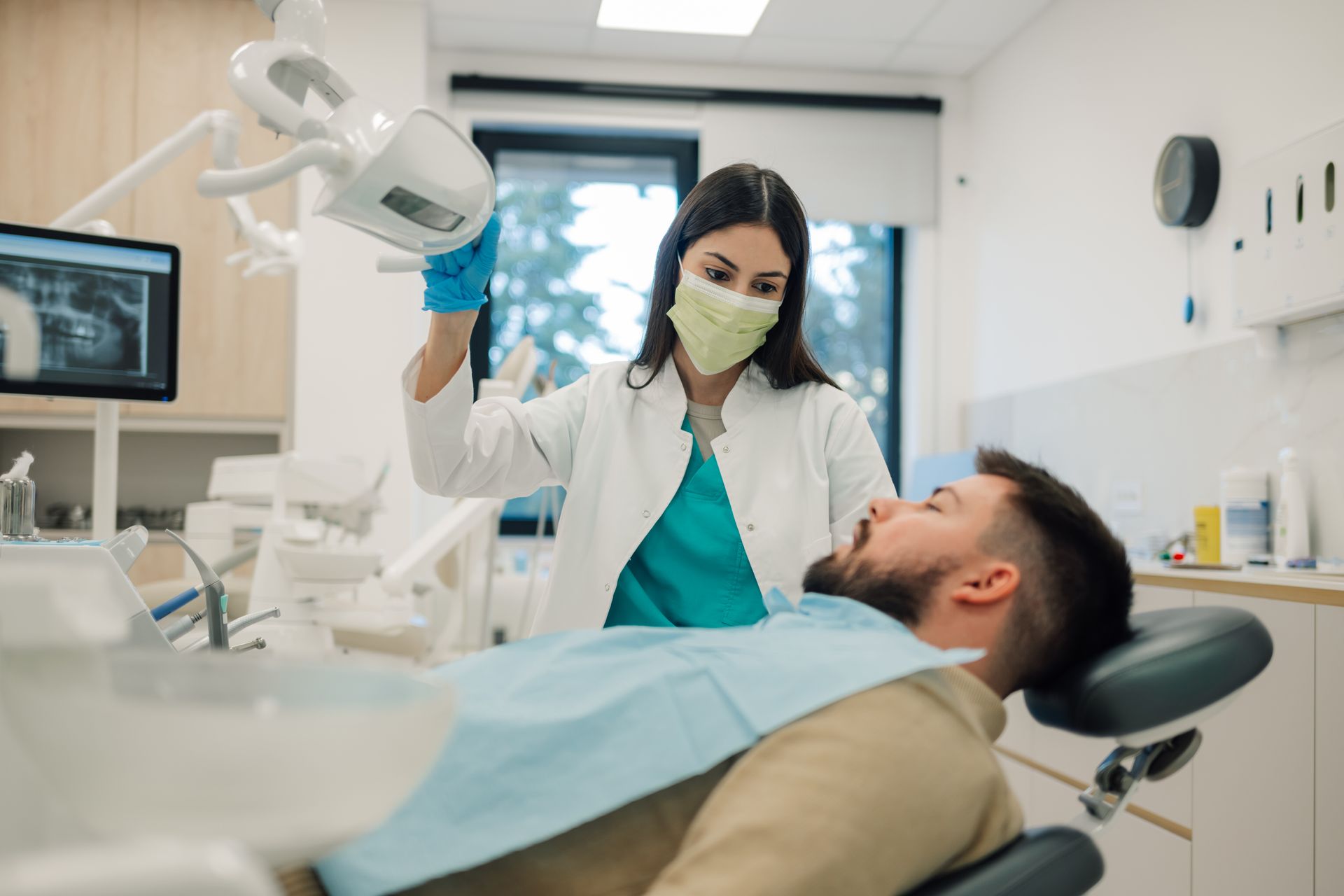Dentist examining a patient in a bright dental clinic, with a dental light and monitor nearby