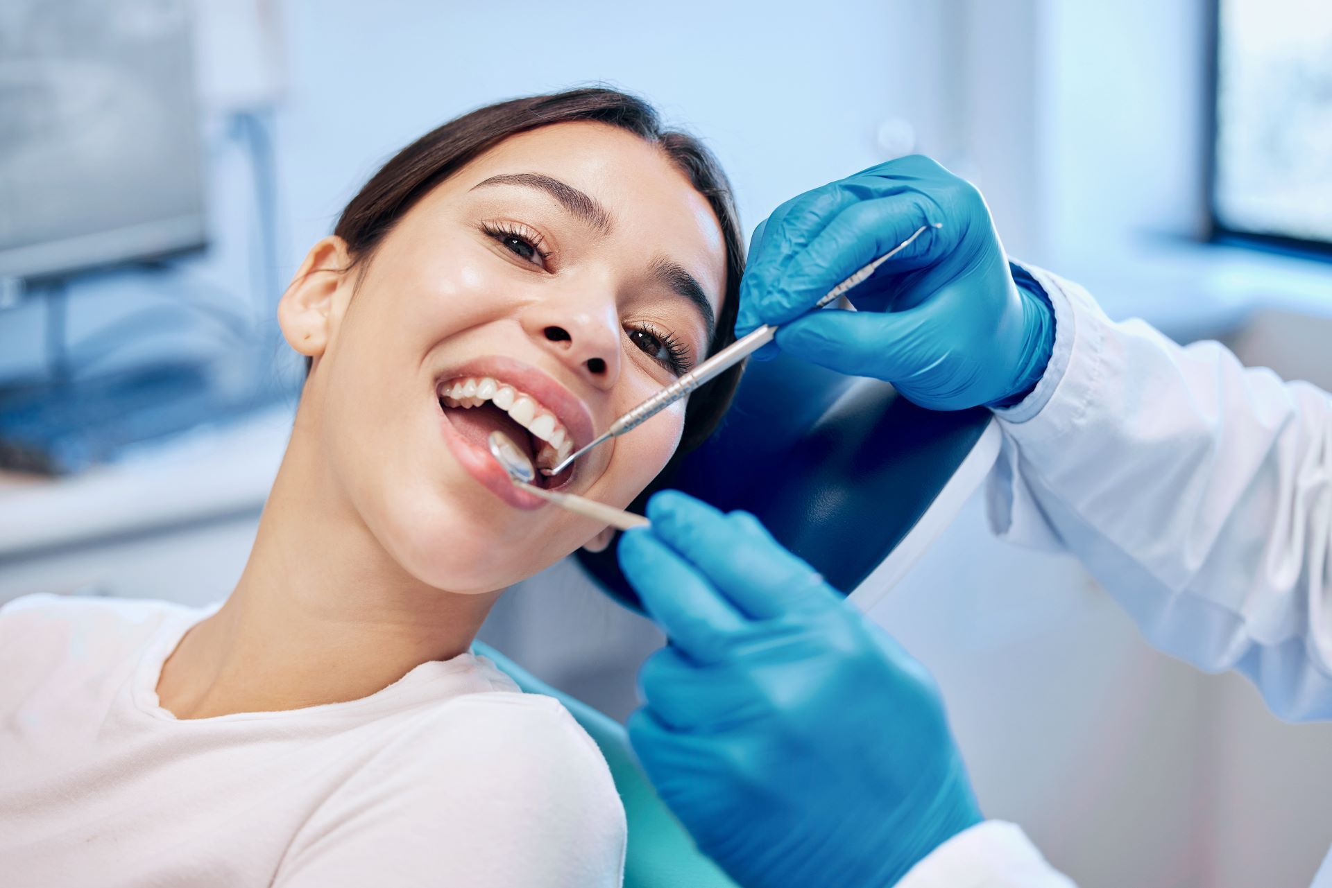 Dentist examining a smiling patient’s teeth with dental tools in a clinic