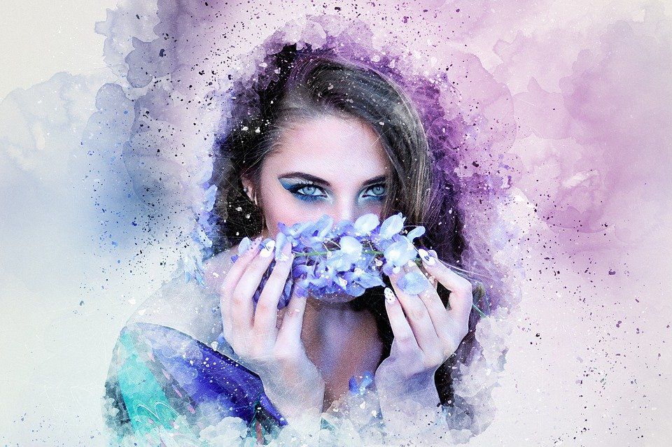 Woman with blue eyes holding purple flowers over her face, surrounded by soft watercolor splashes