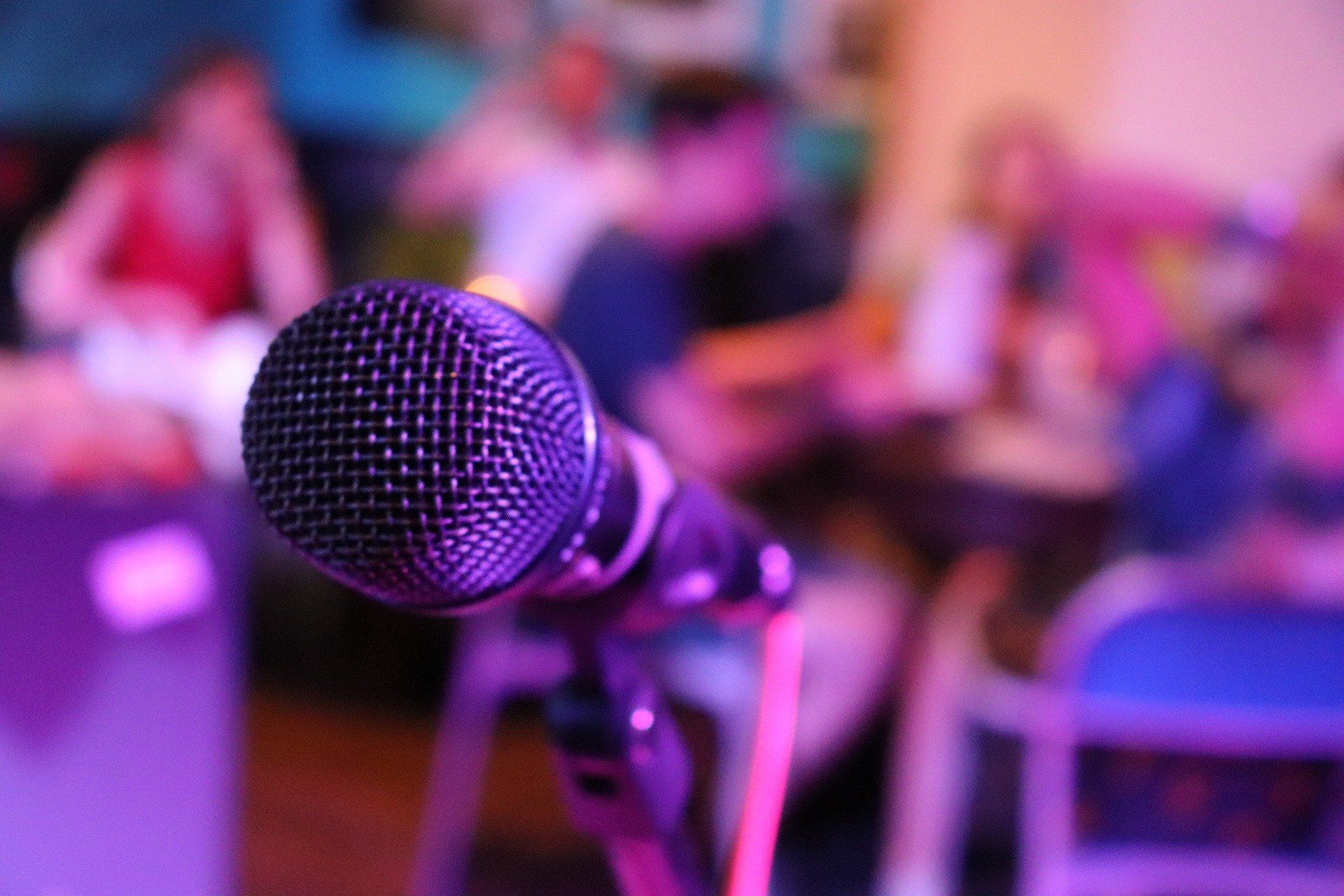 Microphone on a stand in purple stage lighting with a blurred audience in the background