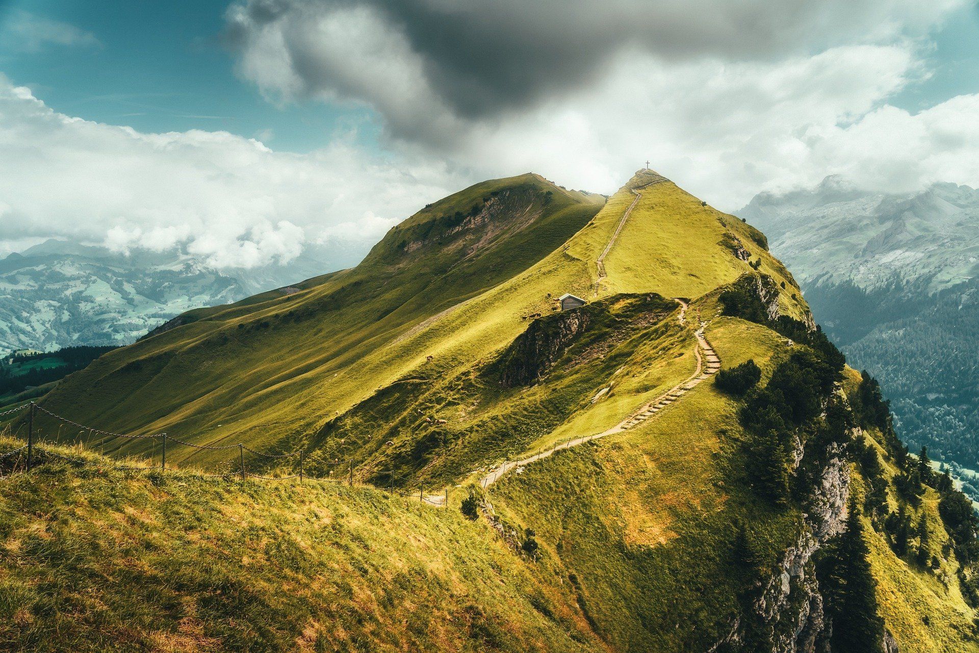 Sunlit mountain ridge with a narrow trail, surrounded by clouds and distant peaks