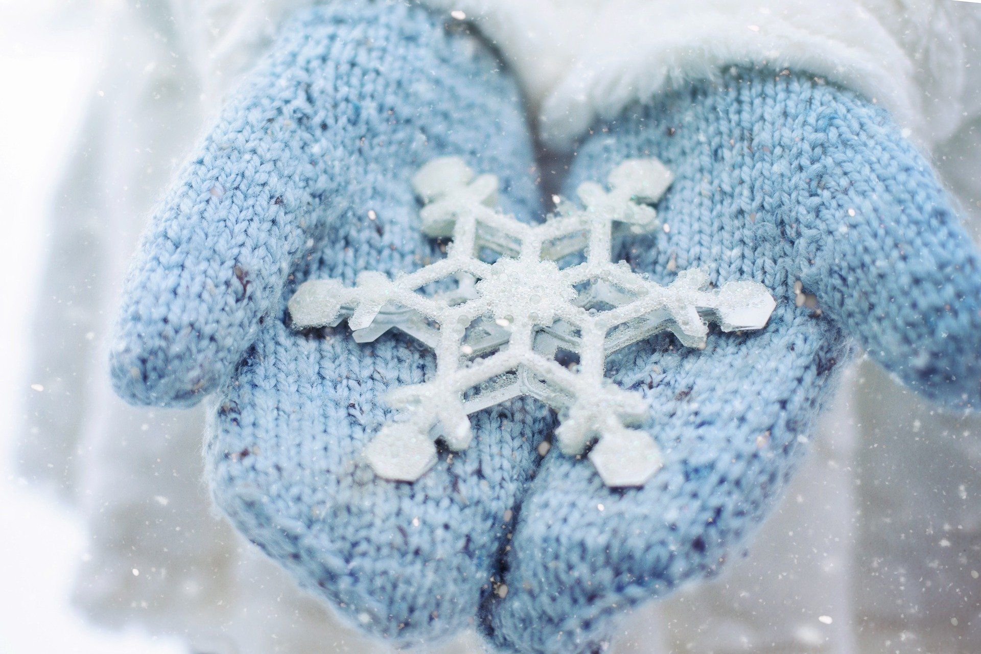 Blue knit gloves holding a white snowflake in falling snow
