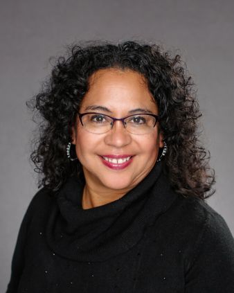 A woman wearing glasses and a black sweater is smiling for the camera.
