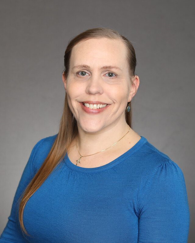 A woman in a blue shirt is smiling for the camera.