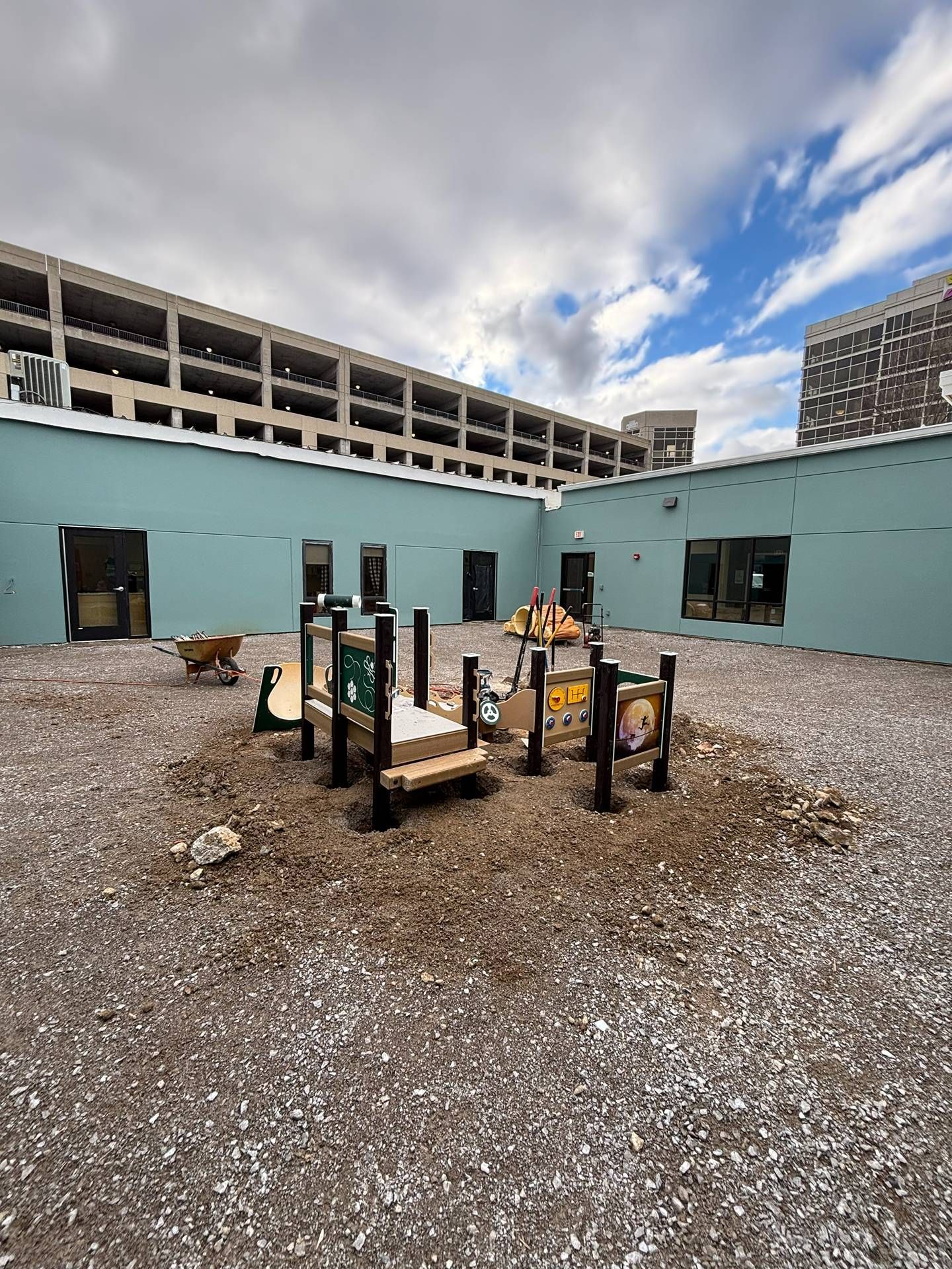 Empty gravel courtyard with a small playground and light blue building under a cloudy sky