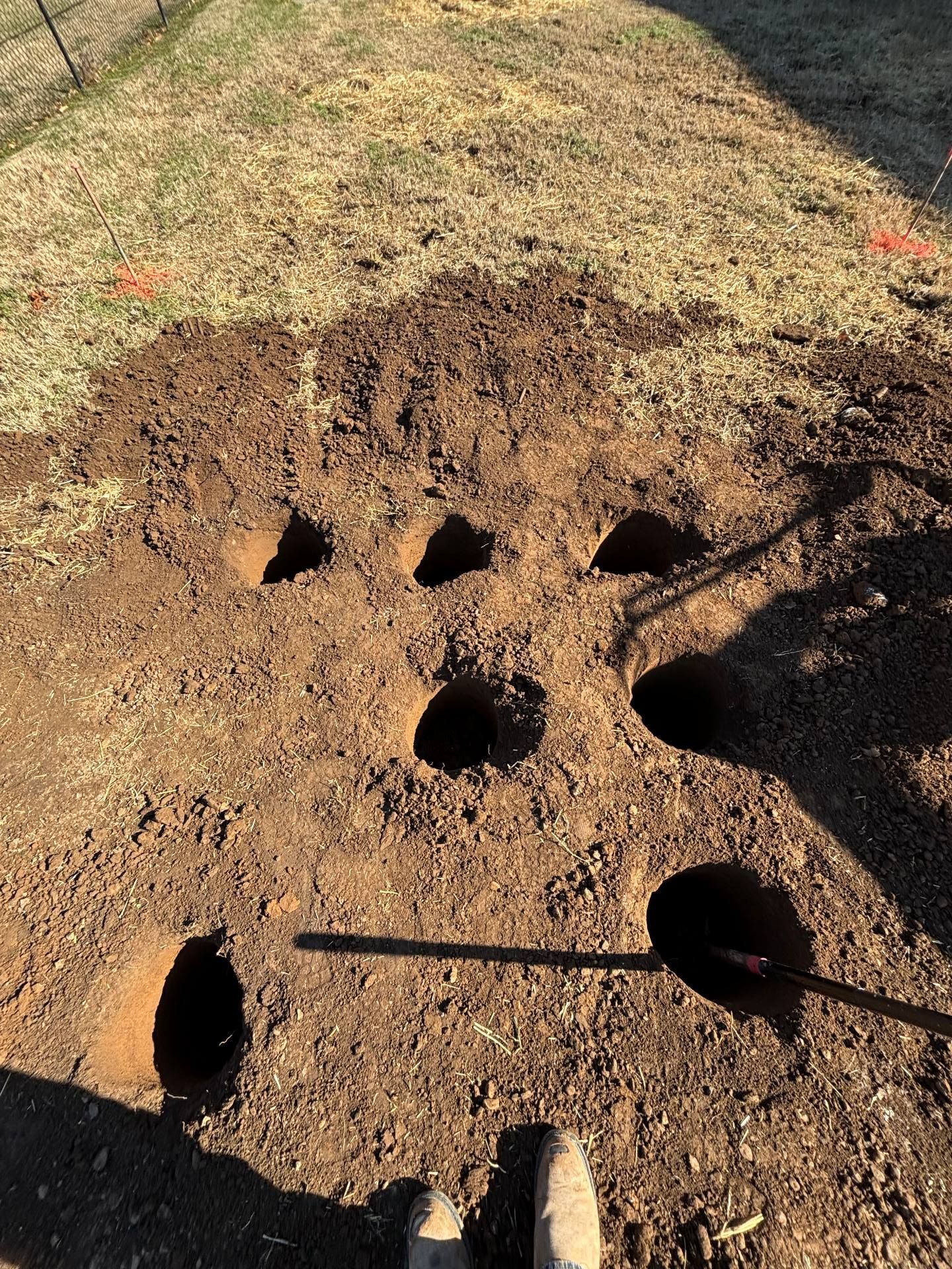 Rectangular dirt mound with several round holes and one crosswise stick in a grassy outdoor area
