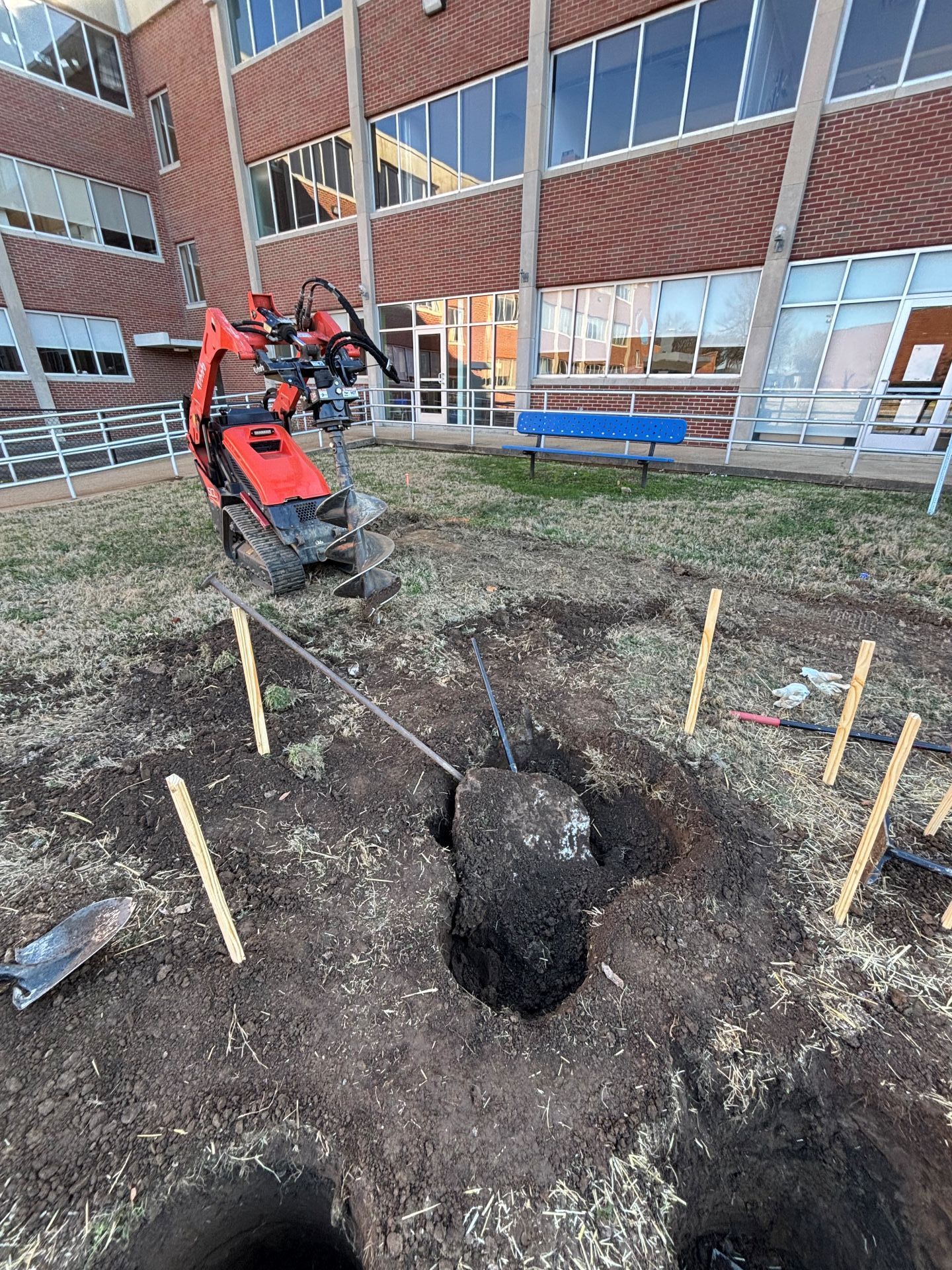 Mini excavator at a construction site beside a large hole, with wooden stakes marking the area.
