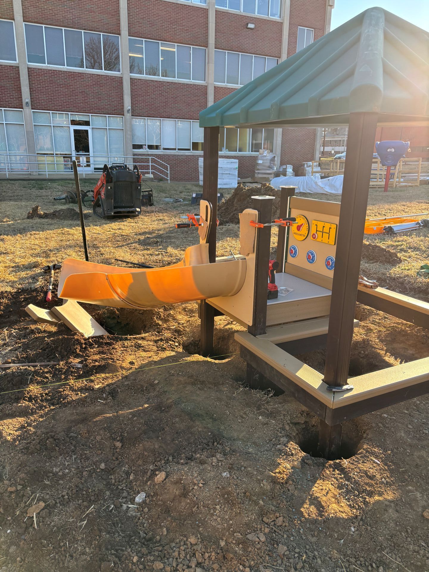 Outdoor playground slide with orange tube and green roof beside a brick building