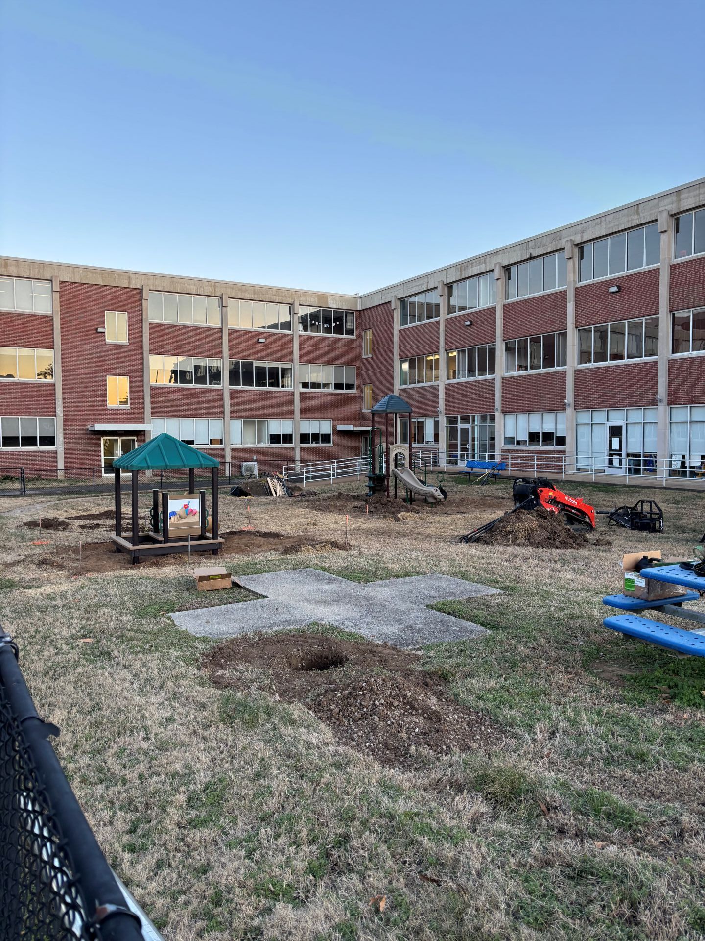 School playground with a play structure, slide, and construction equipment in front of a brick building