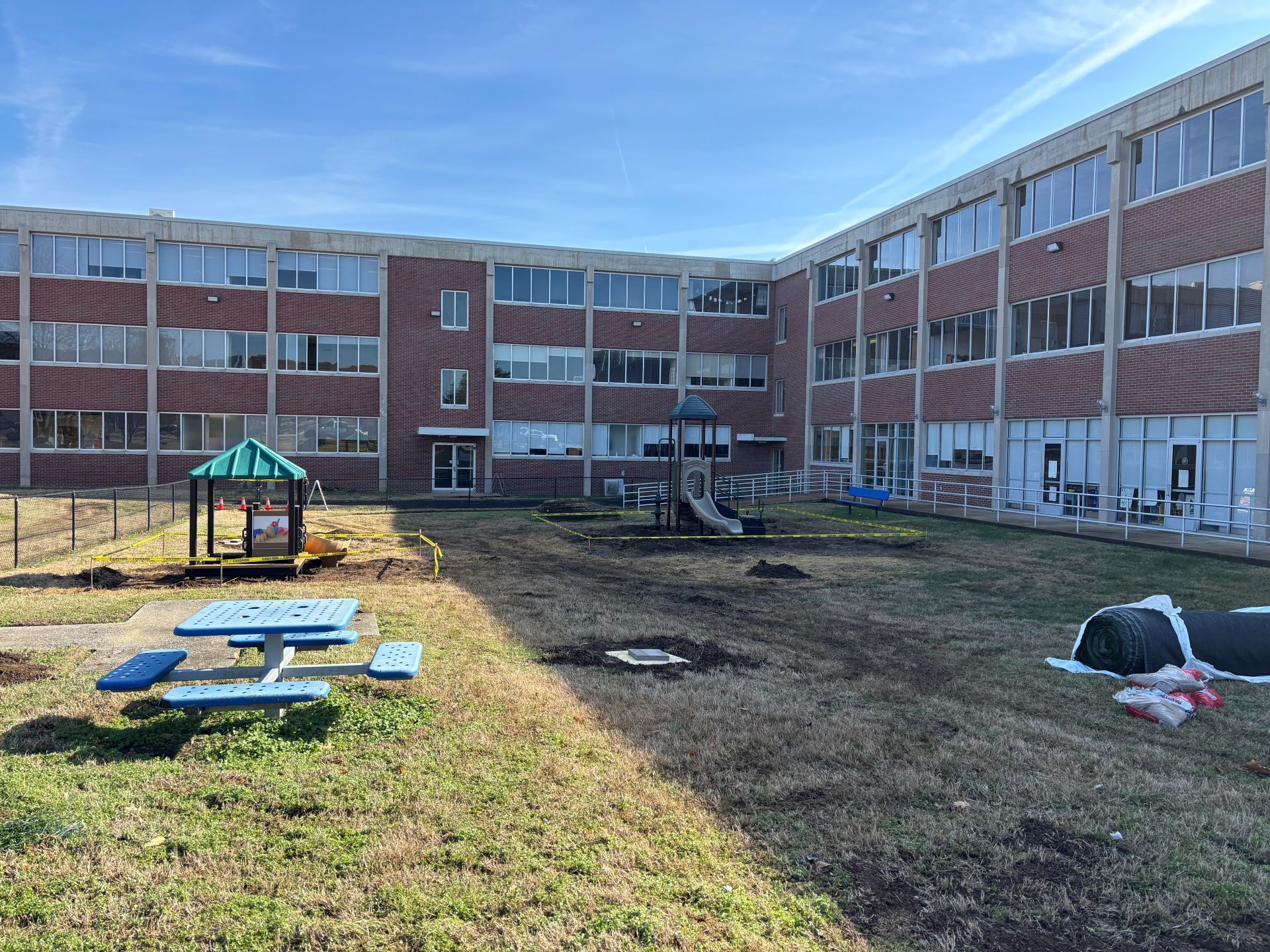 Courtyard between apartment buildings with a picnic table, small playground, and patchy grass in daylight