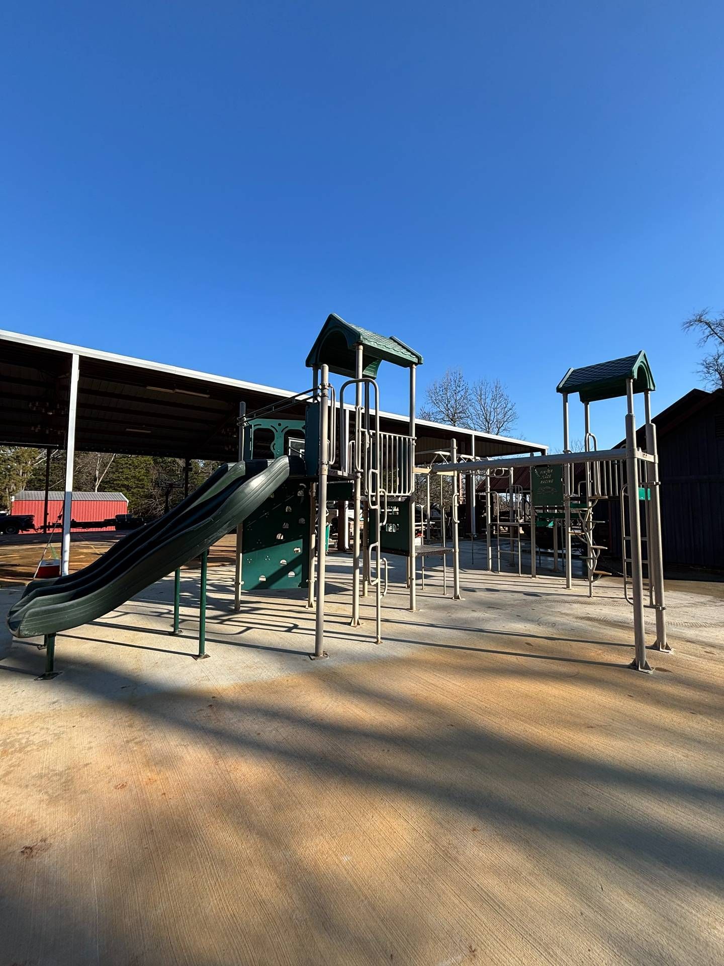 Empty playground with green slides and climbing structures under a clear blue sky.
