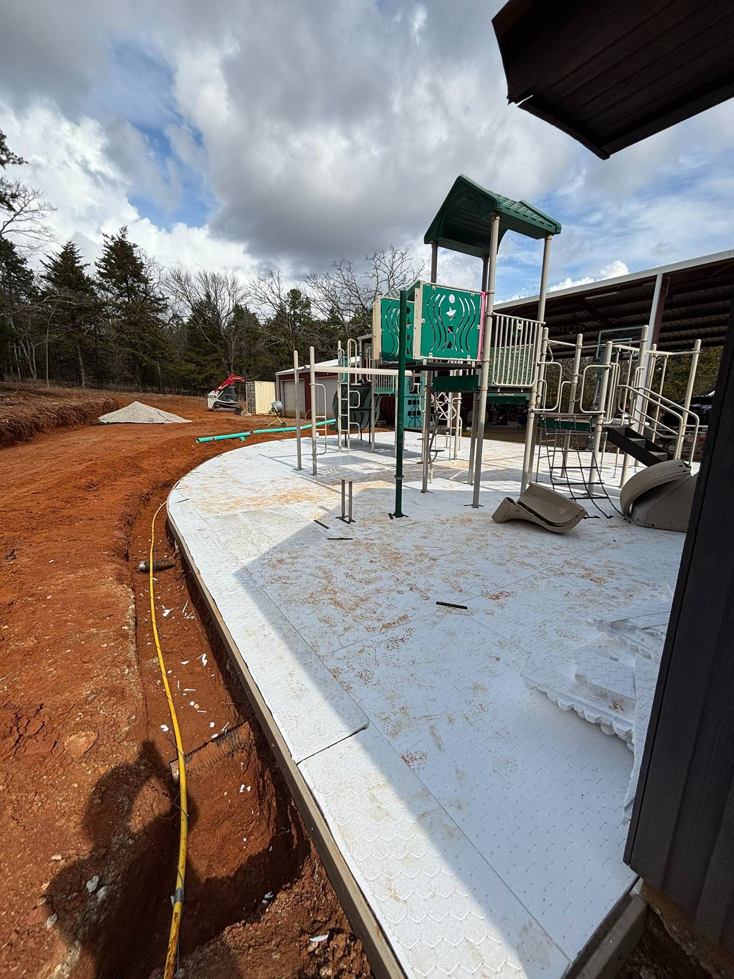 New building under construction with concrete slab, support posts, and cloudy sky over wooded site