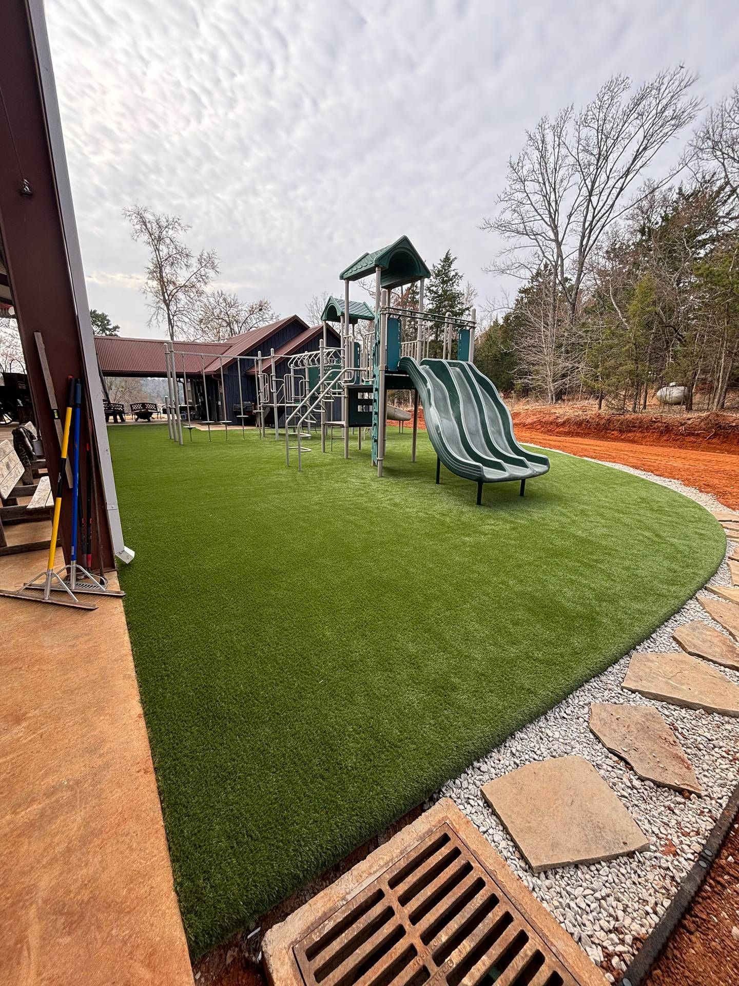 Playground with green turf, two slides, and curved stone path beside trees