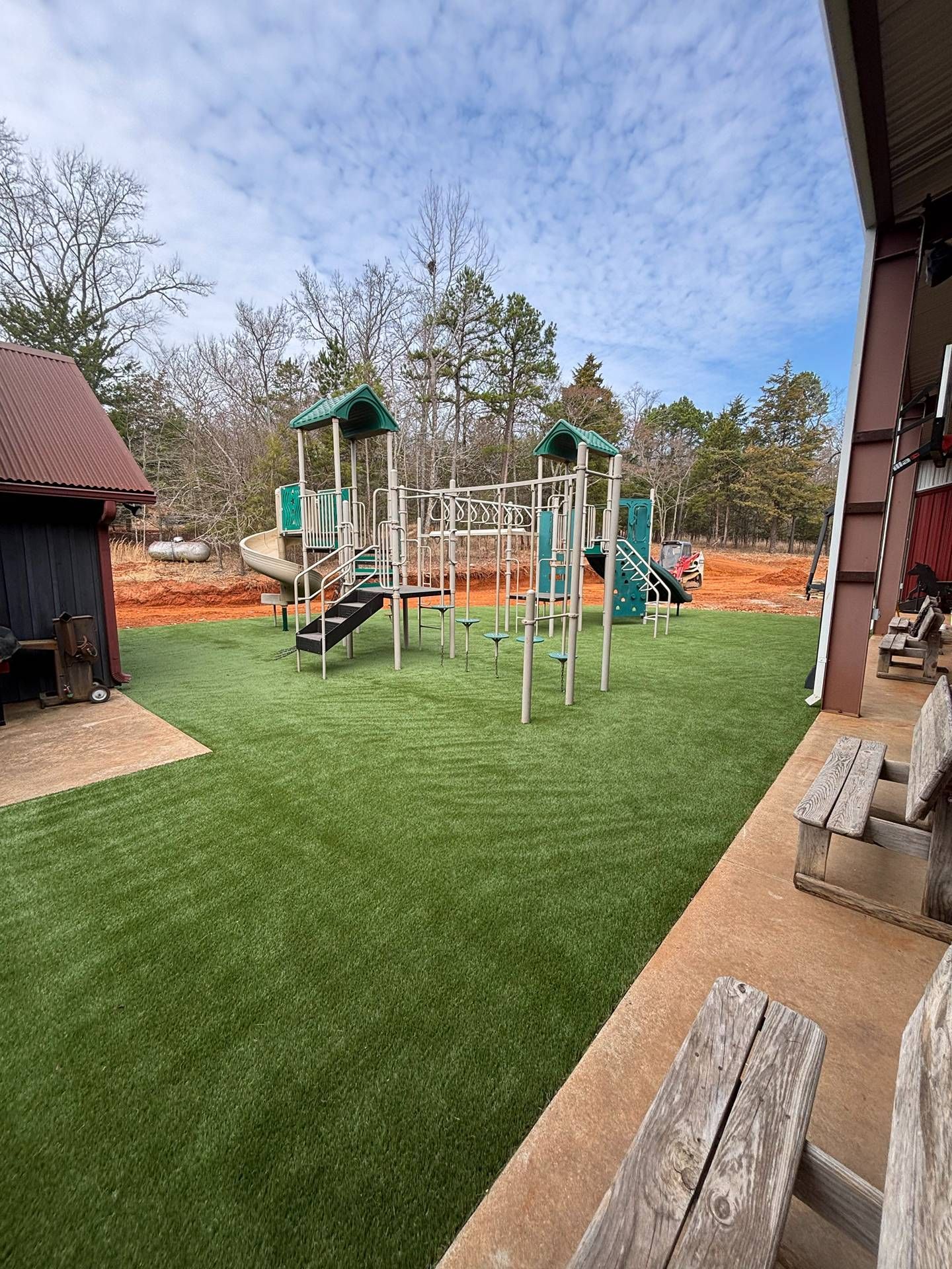 Outdoor playground with green turf, climbing equipment, and a slide beside a brick building.