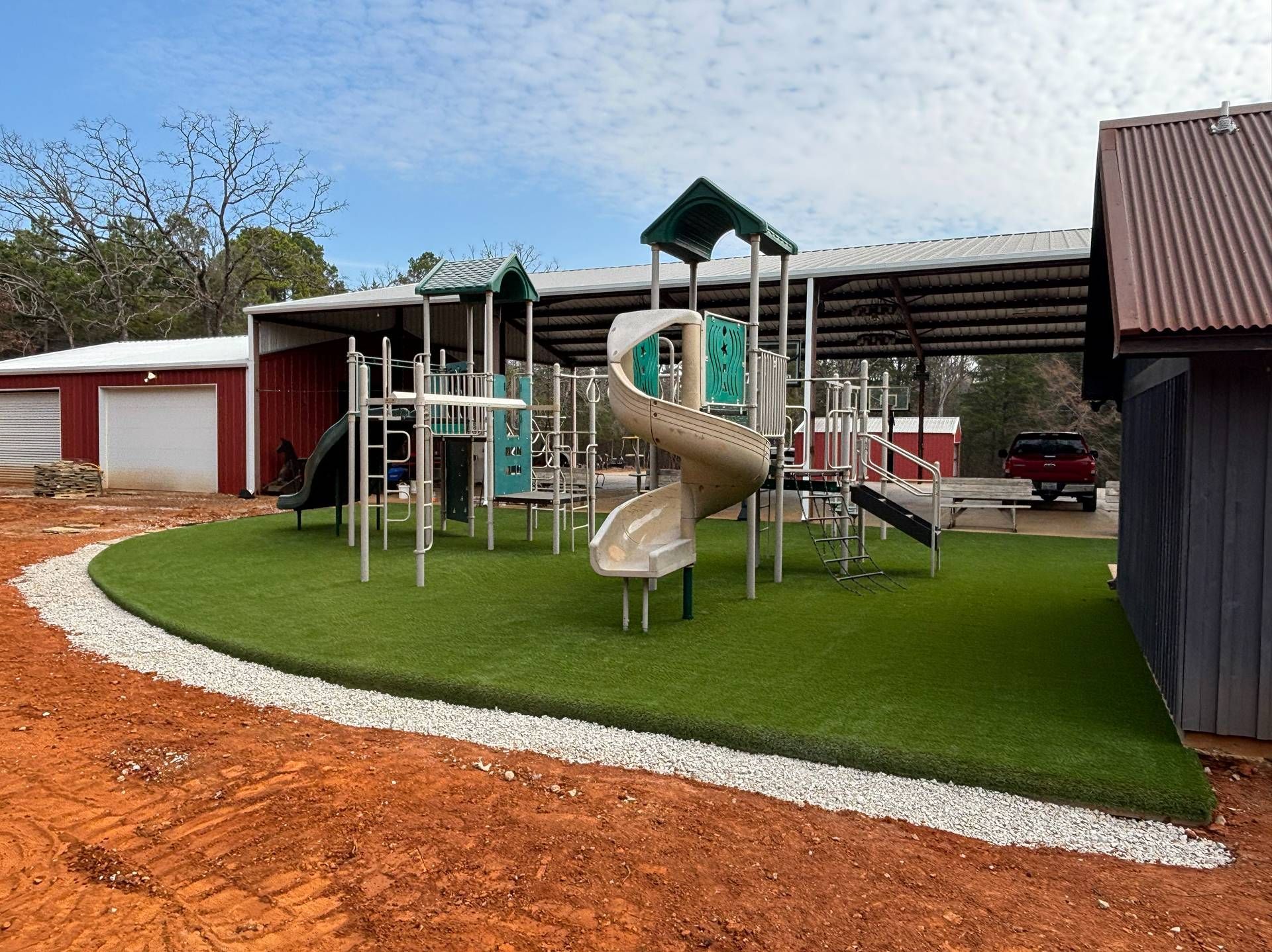 Outdoor playground with tan slide, metal climbing frame, and green turf beside red buildings