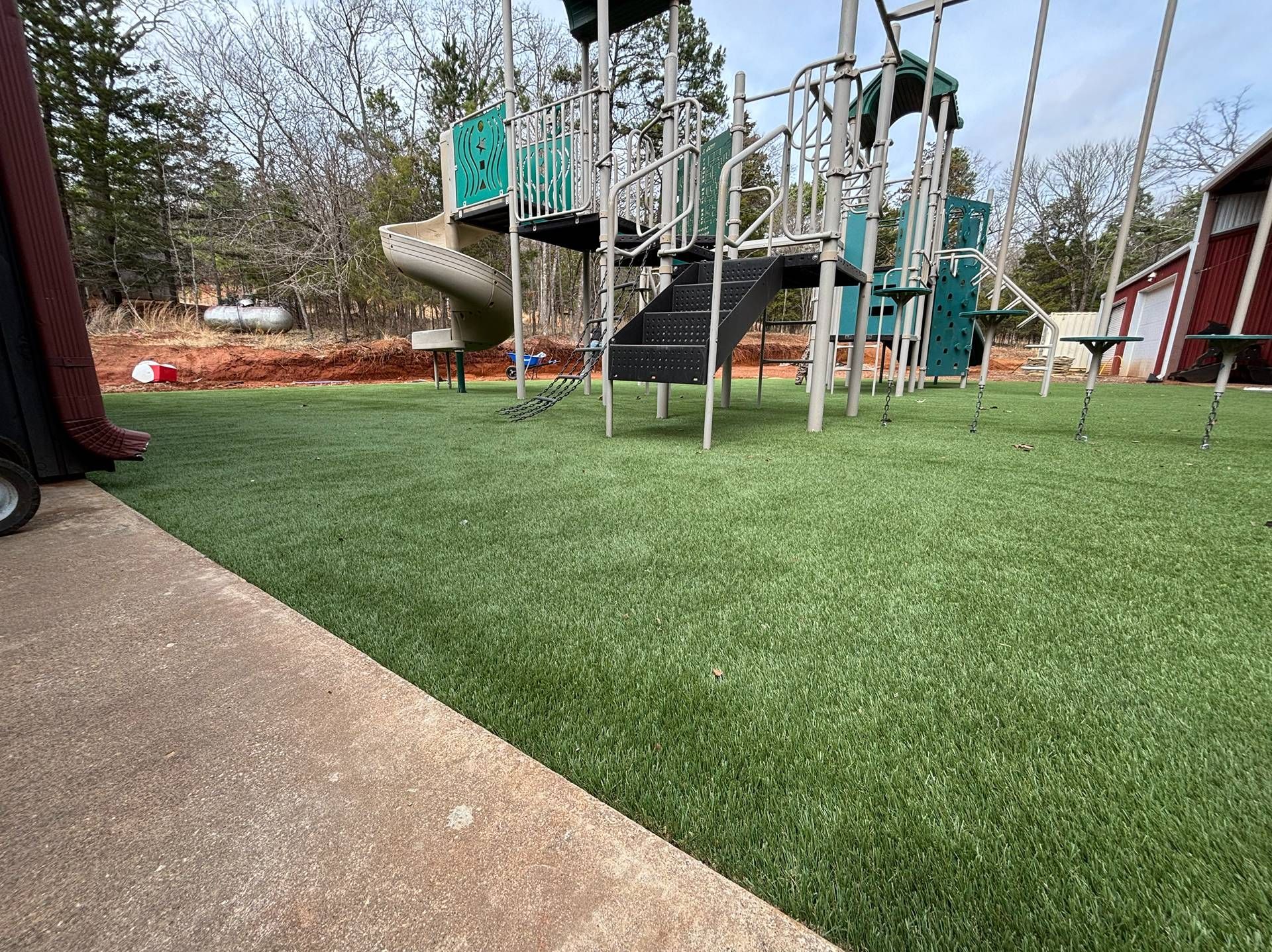 Playground with artificial turf, climbing ropes, and a slide under a cloudy sky