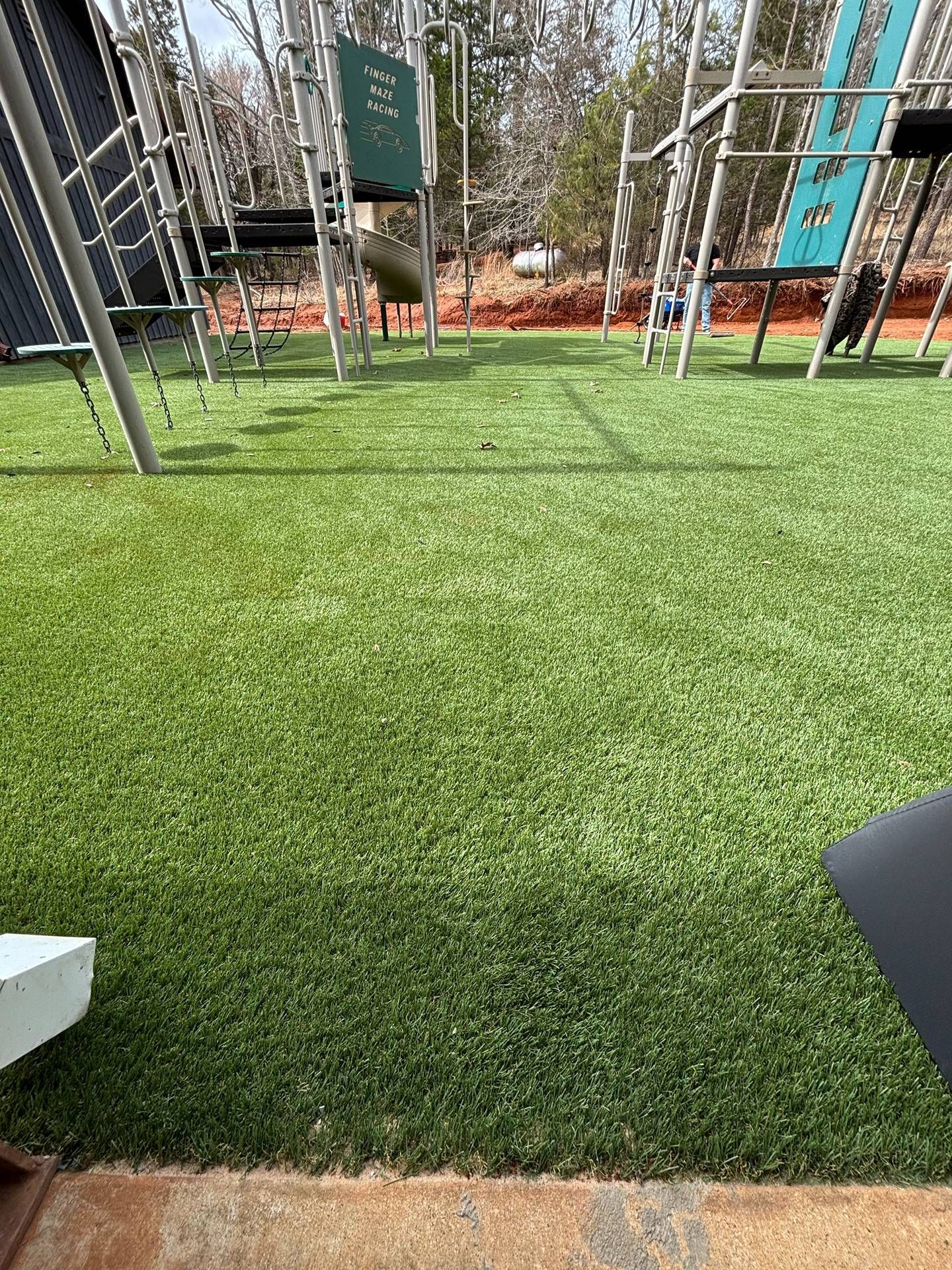 Artificial turf field with metal playground or fitness structures and trees in the background