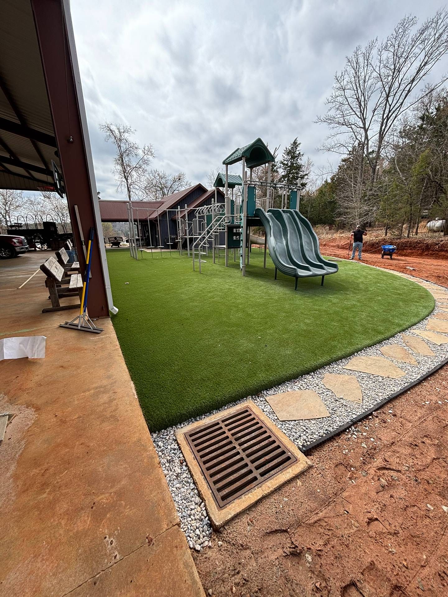 Playground with slides and climbing structure beside a green turf area and building on an overcast day