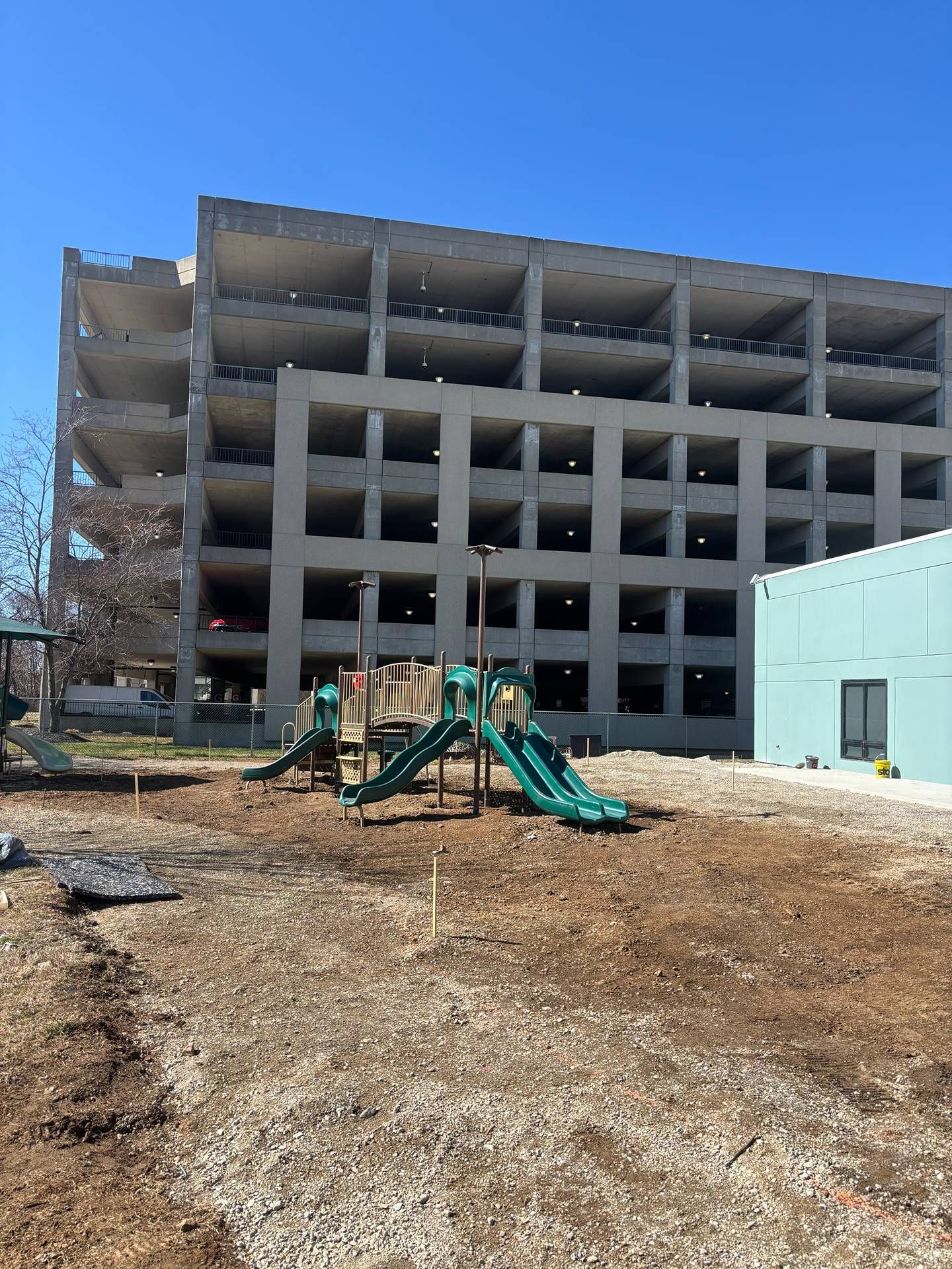 Partially demolished concrete building with a green excavator in front under a clear blue sky