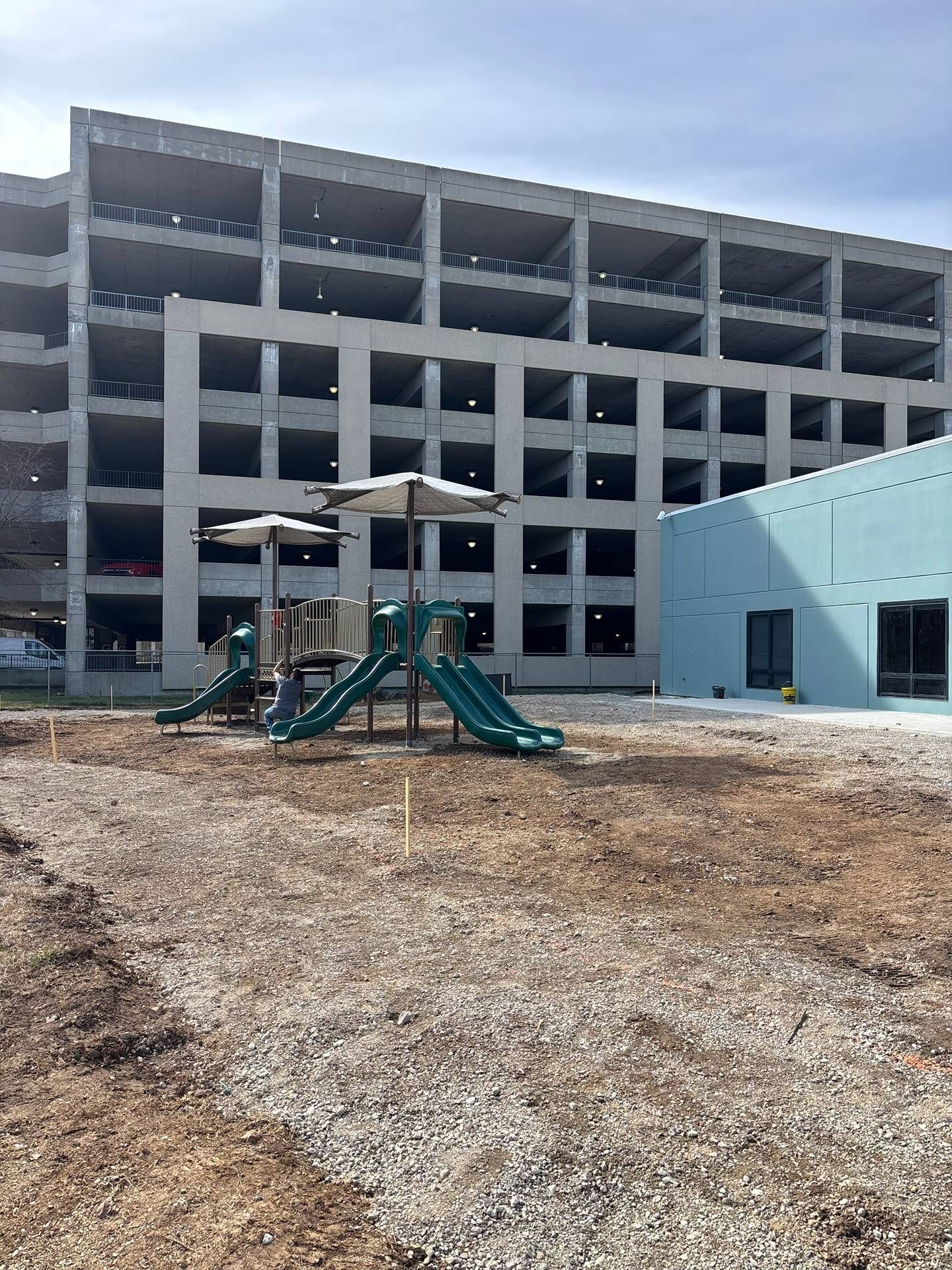 Empty playground in front of a gray concrete building with a teal play structure