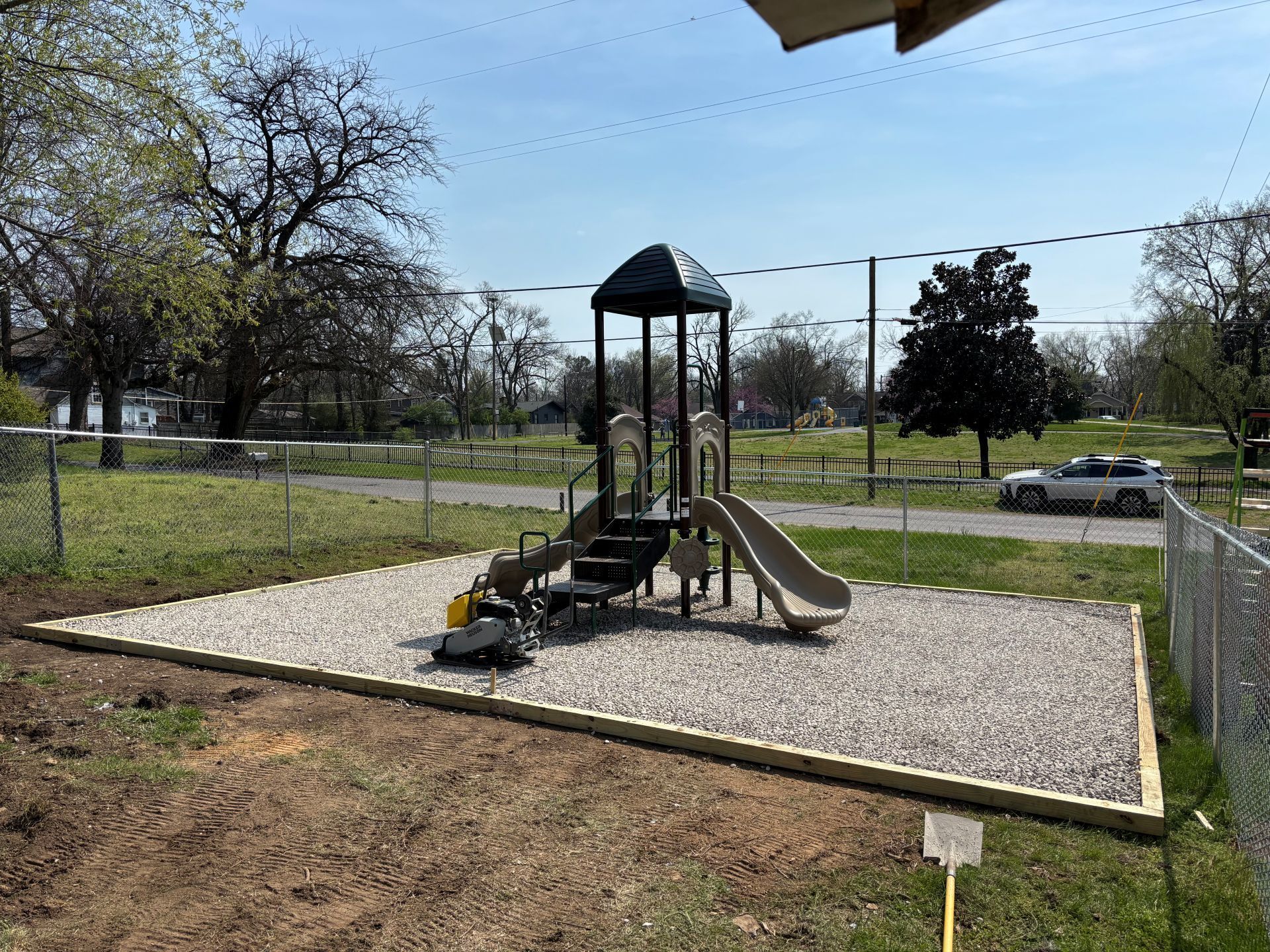 Small playground with slide and climbing frame on a gravel pad in a grassy park.