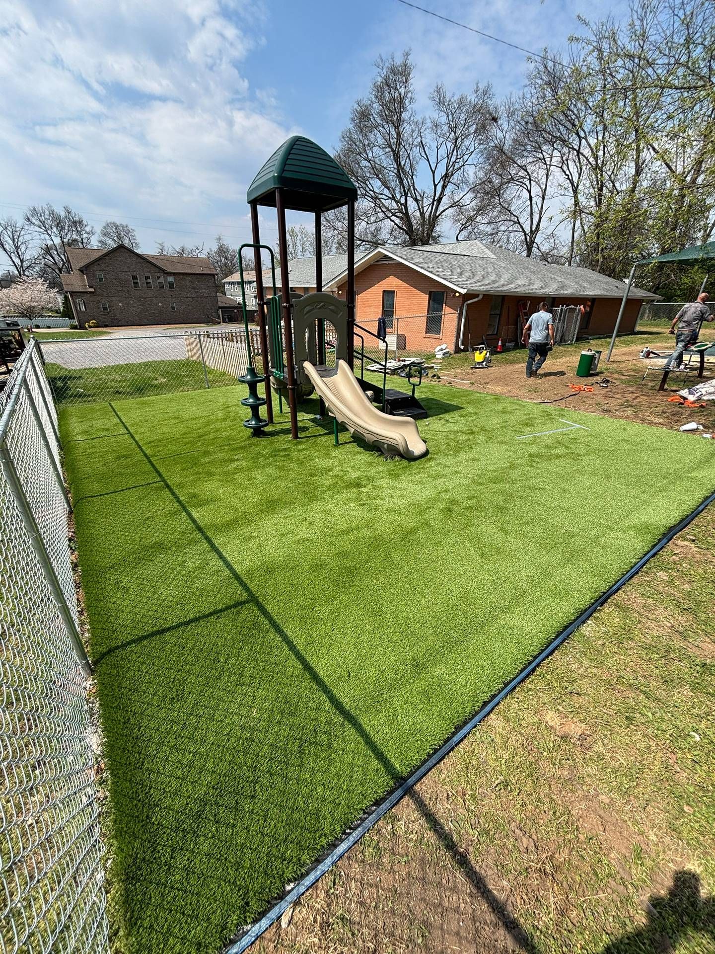 Backyard playground with green turf, climbing tower, and tan slides under a sunny sky