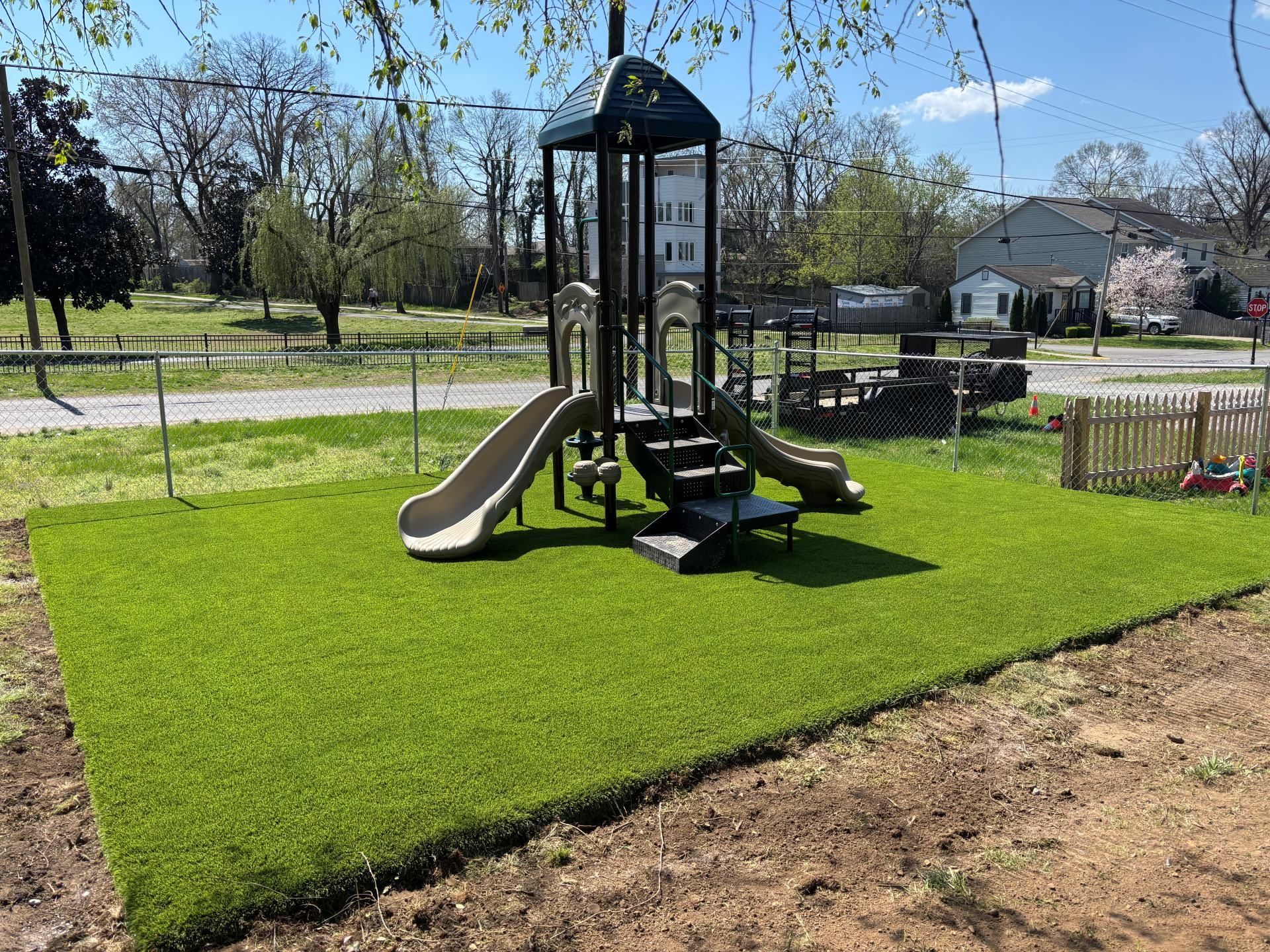 Small playground structure with slides on a bright green lawn in a quiet park.