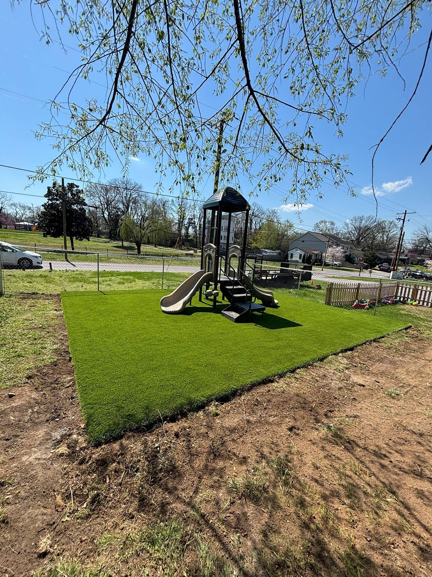 Playground with slide and climbing structure on a bright green turf pad under a clear blue sky.