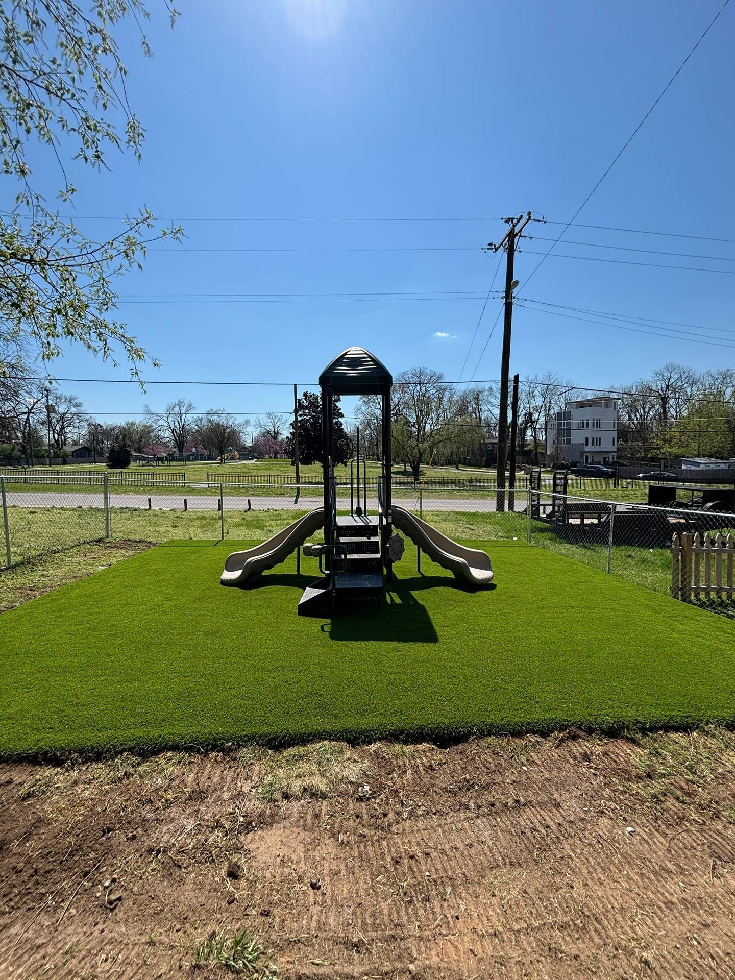 Empty playground slide on green grass under a clear blue sky