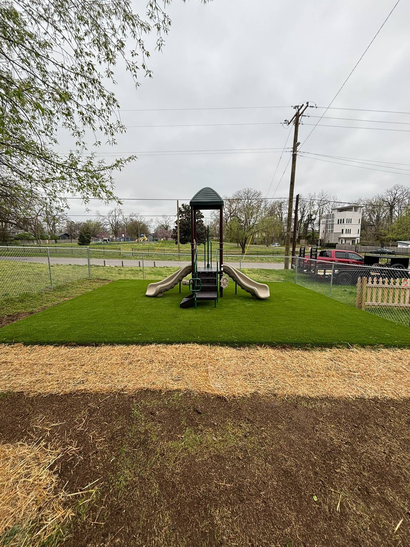 Playground slide and climbing structure on a grassy park lawn under a cloudy sky