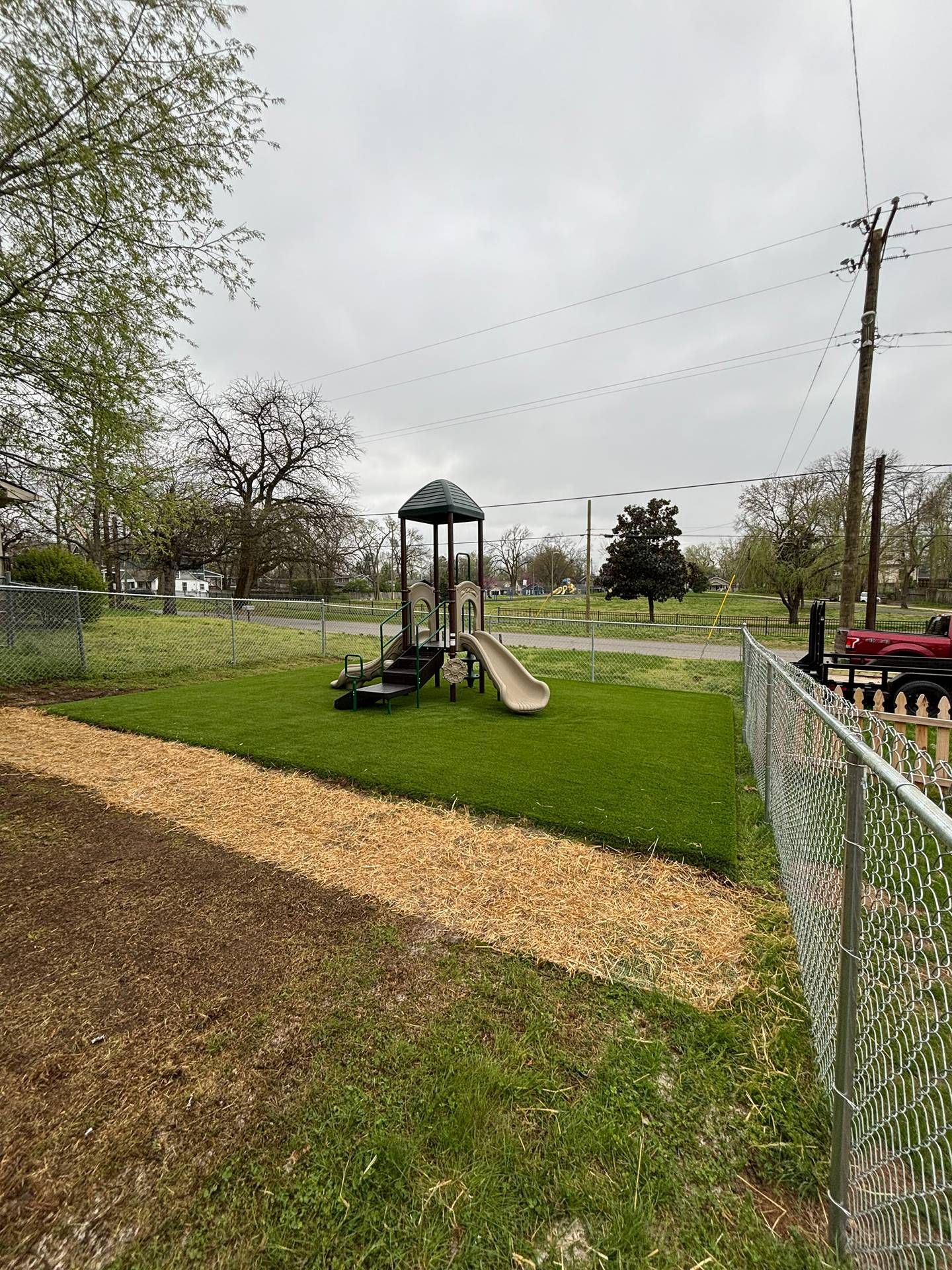 Empty playground with slide and climbing tower beside a fence on a cloudy day