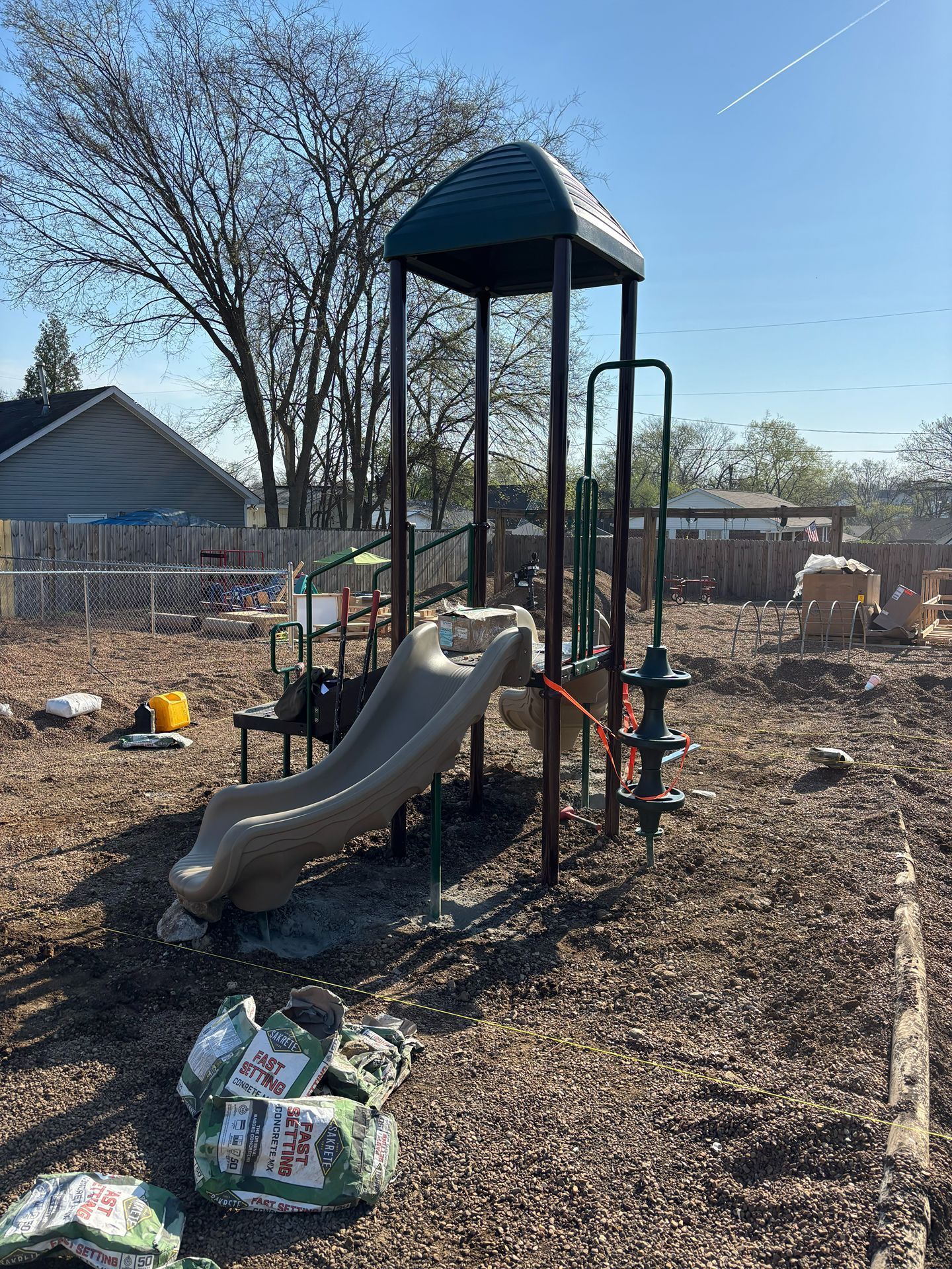 Playground climbing structure with slide and ladder in a dry backyard, under a clear blue sky.