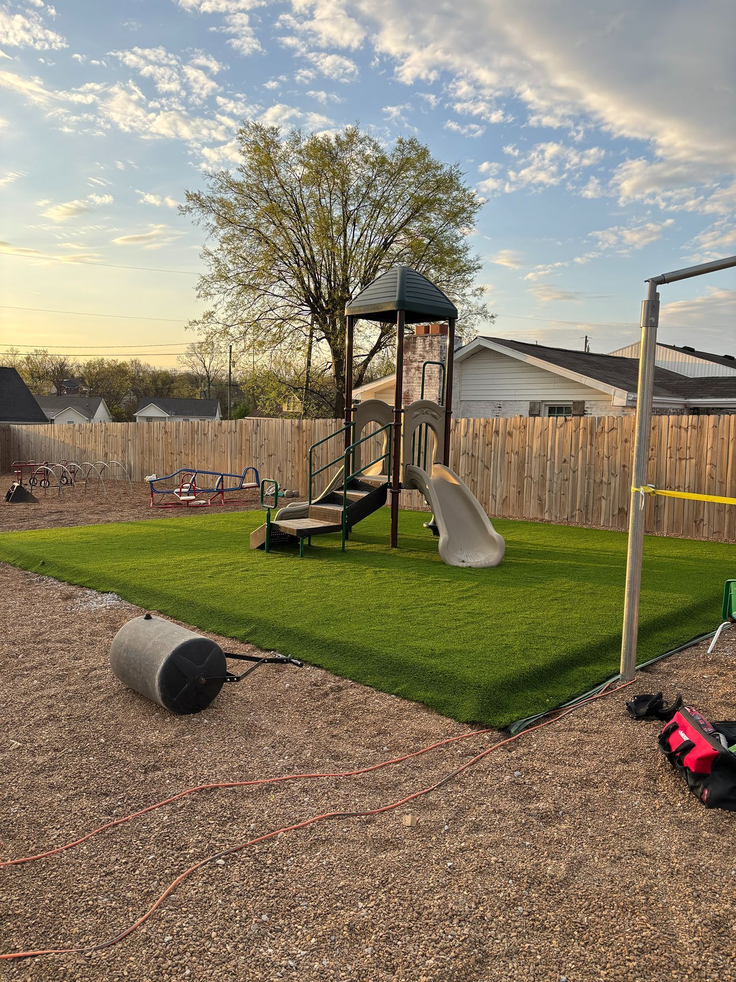 Backyard playground with slide, swing, tree, and gravel area at sunset