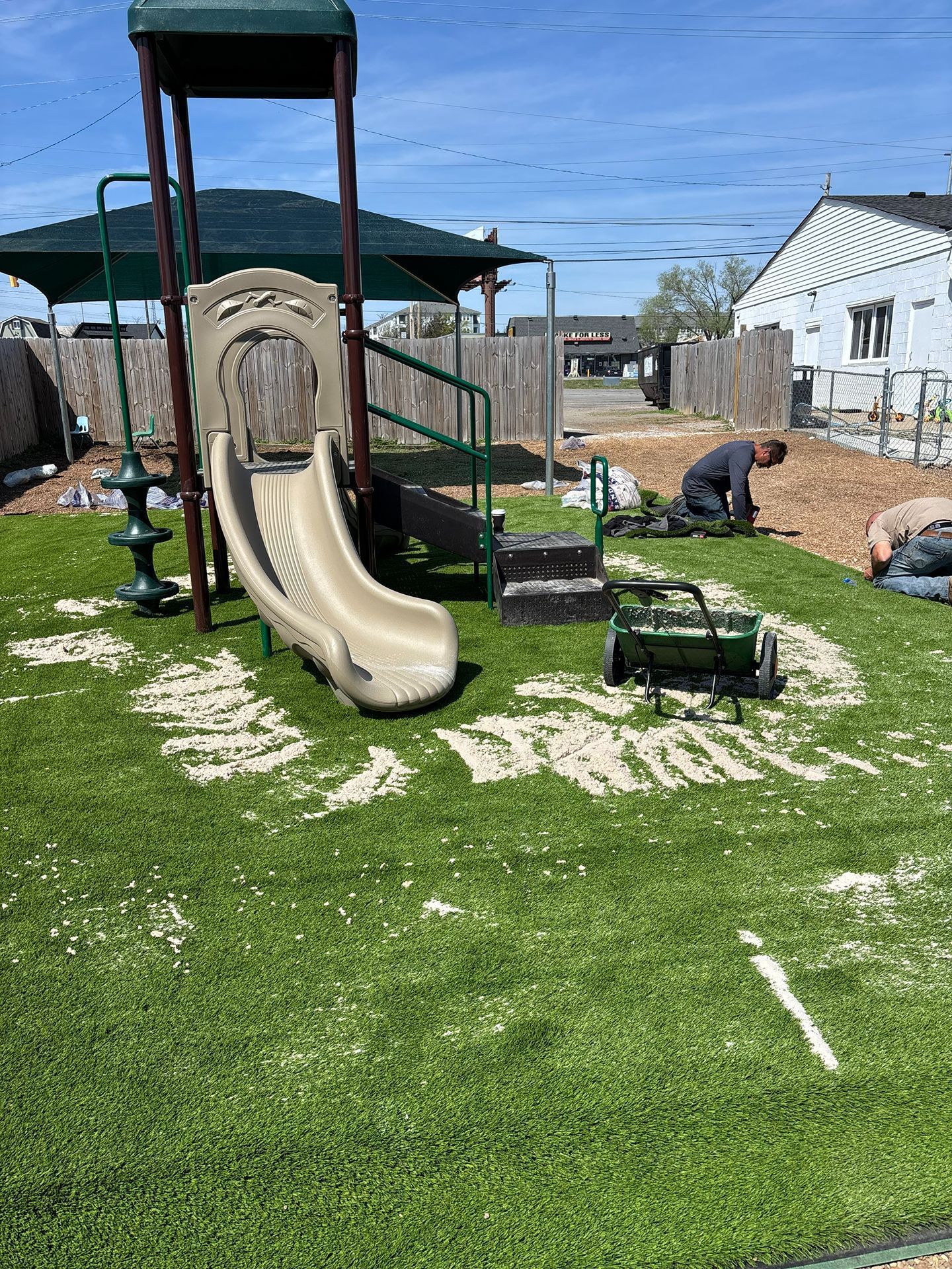 Backyard playground with tan slide, green turf, and a play canopy on a sunny day