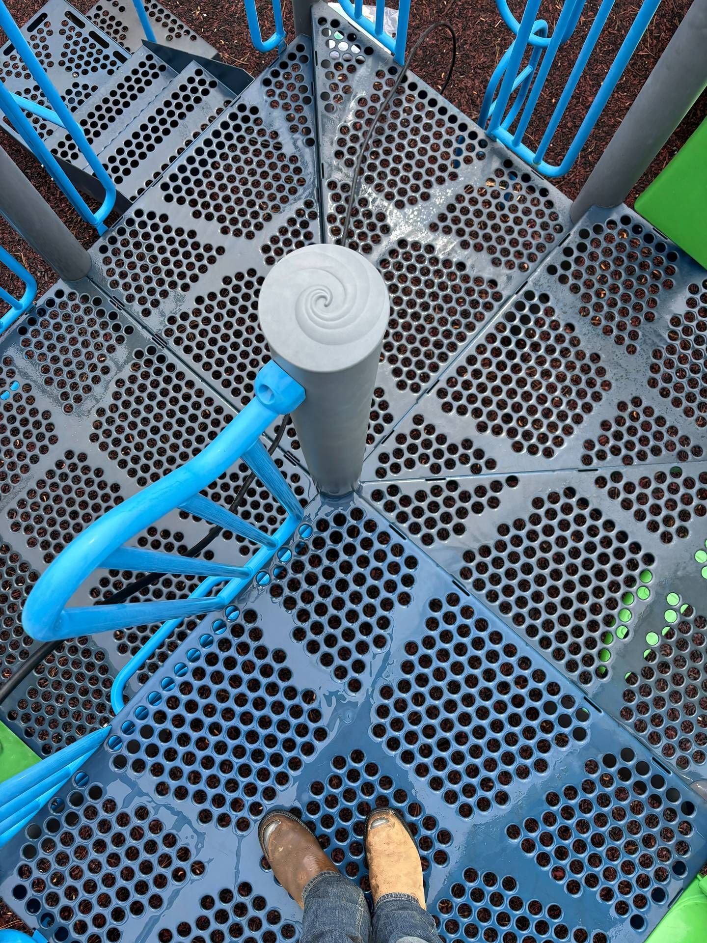 Top-down view of a blue metal spiral staircase with perforated steps and a gray center post